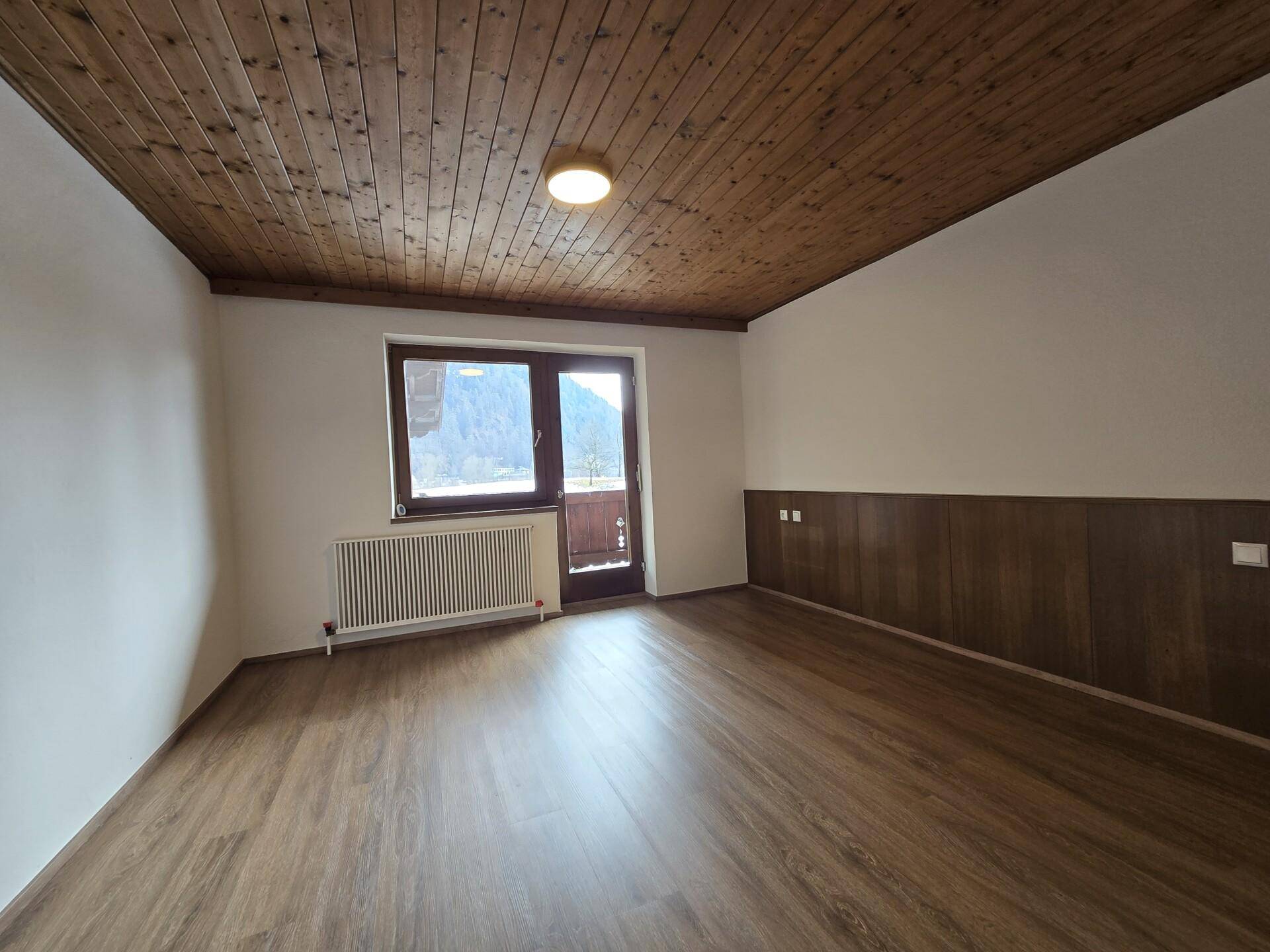 Schlafzimmer mit Laminatboden, Holzbalkendecke und Zugang zum Balkon.