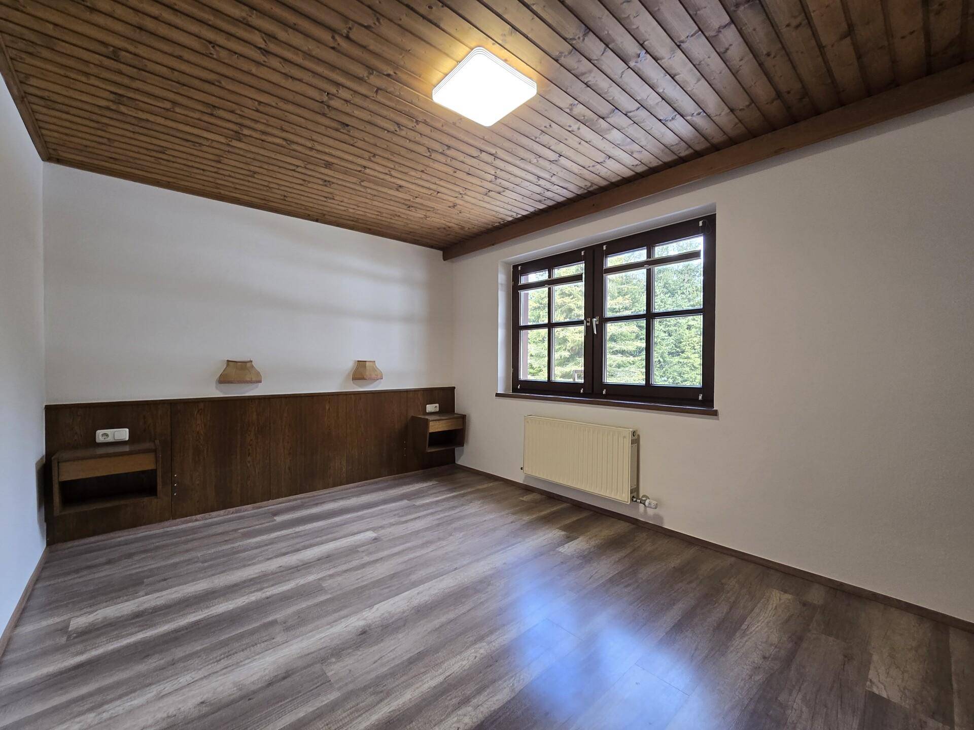 Schlafzimmer mit Holzbalkendecke, Laminatboden und Fenster mit Bergblick.