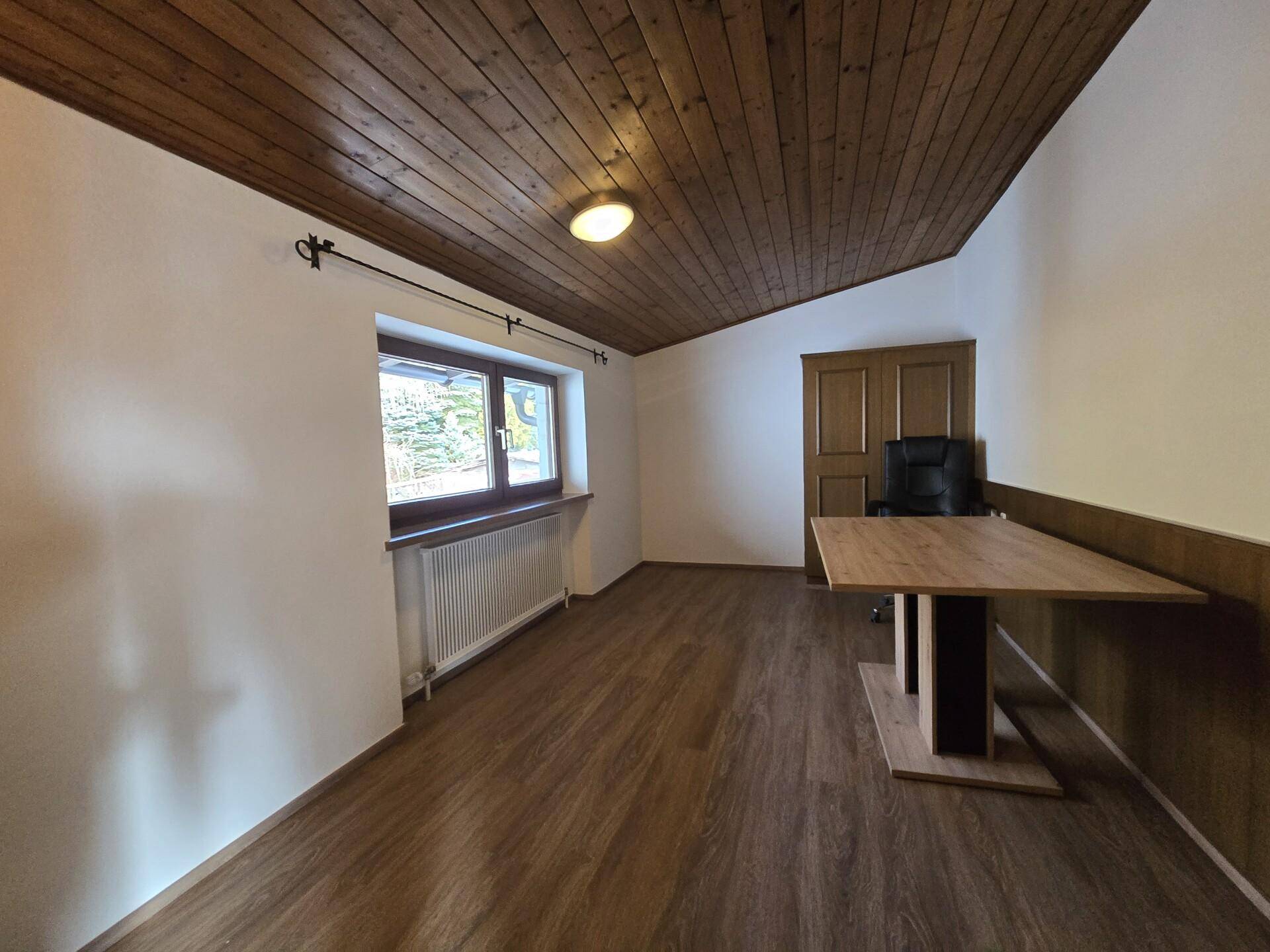 Arbeitszimmer mit Holzbalkendecke, Laminatboden und Schreibtisch.
