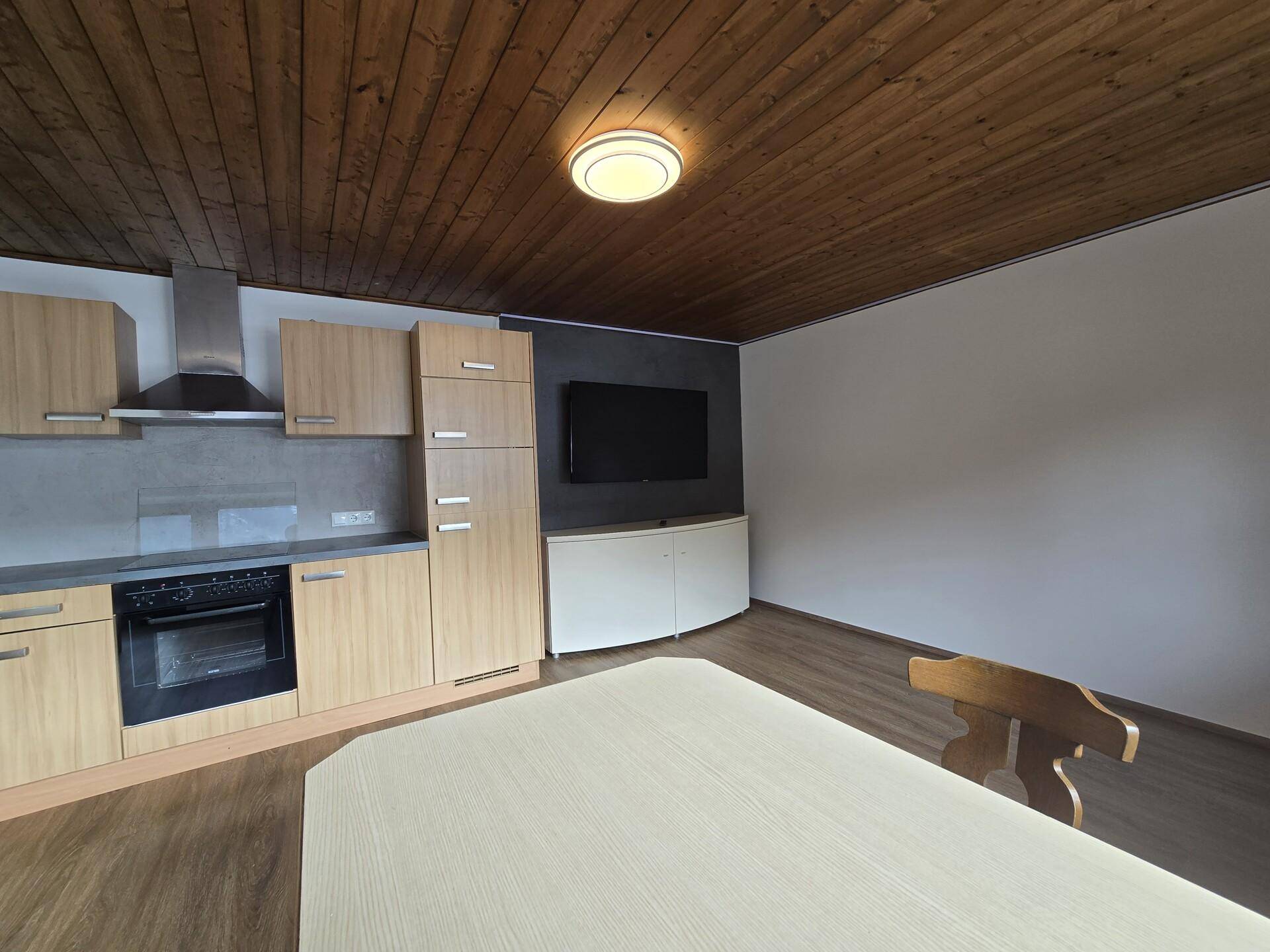 Moderne Küche mit Holzelementen, Essbereich und integriertem Fernseher.
