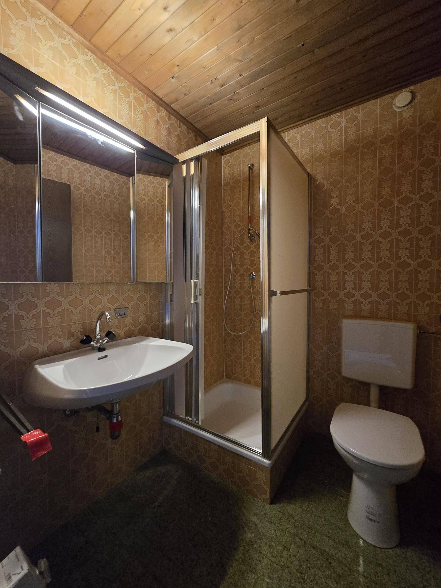 Badezimmer im 80er-Jahre-Stil mit Duschkabine, WC und gemusterten Fliesen.