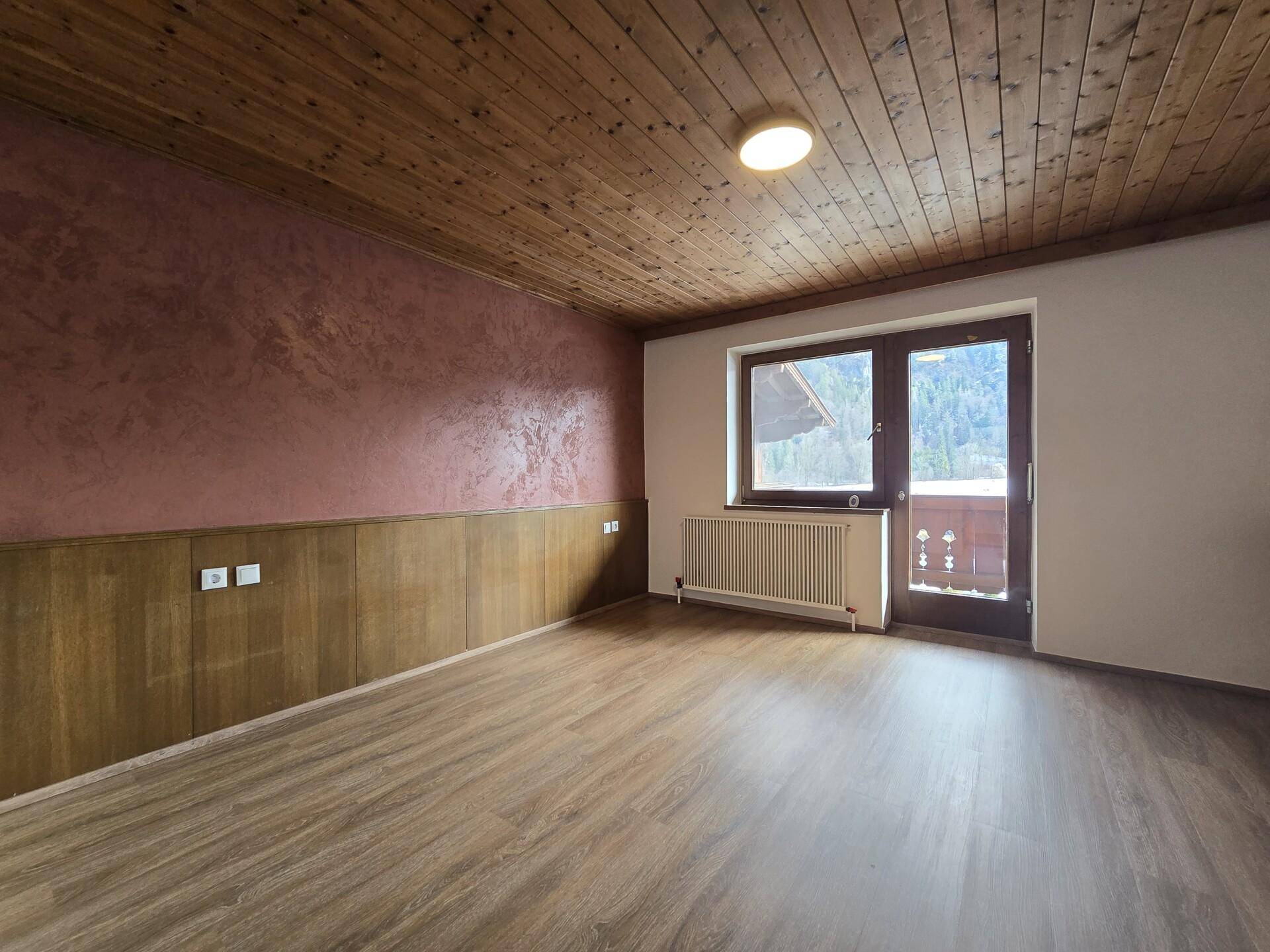 Schlafzimmer mit Laminatboden, Holzbalkendecke und Zugang zum Balkon.