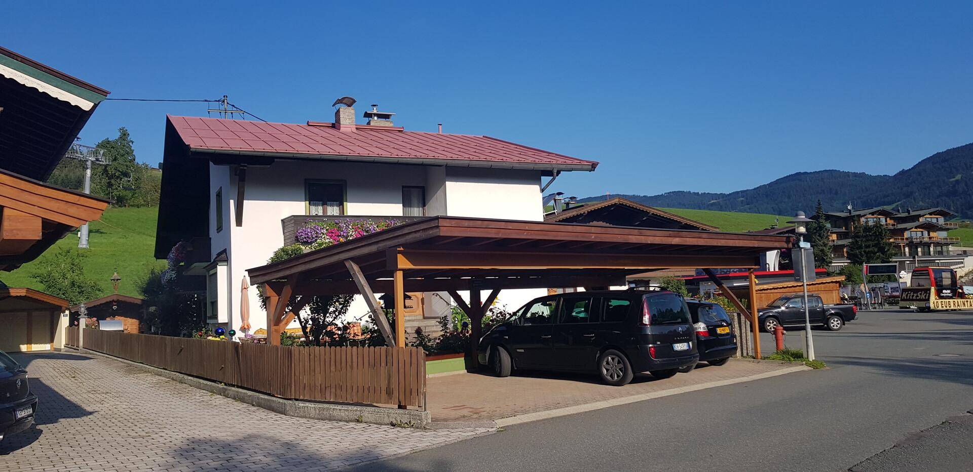 Traditionelles Haus mit rotem Dach und Holzcarport, umgeben von einer bergigen Landschaft.