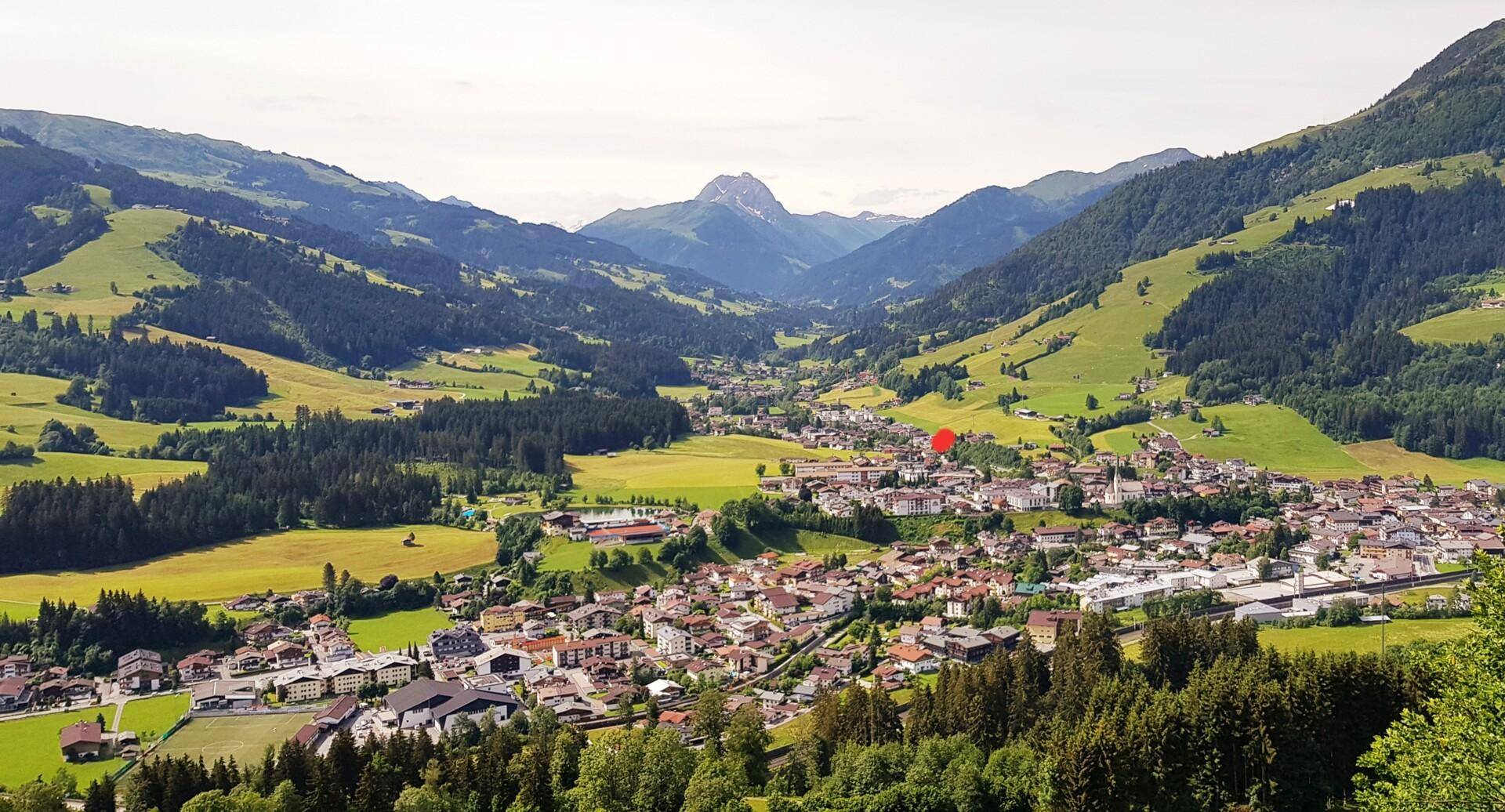 Panoramablick auf eine malerische Stadt im Tal, umgeben von grünen Hügeln und majestätischen Bergen.