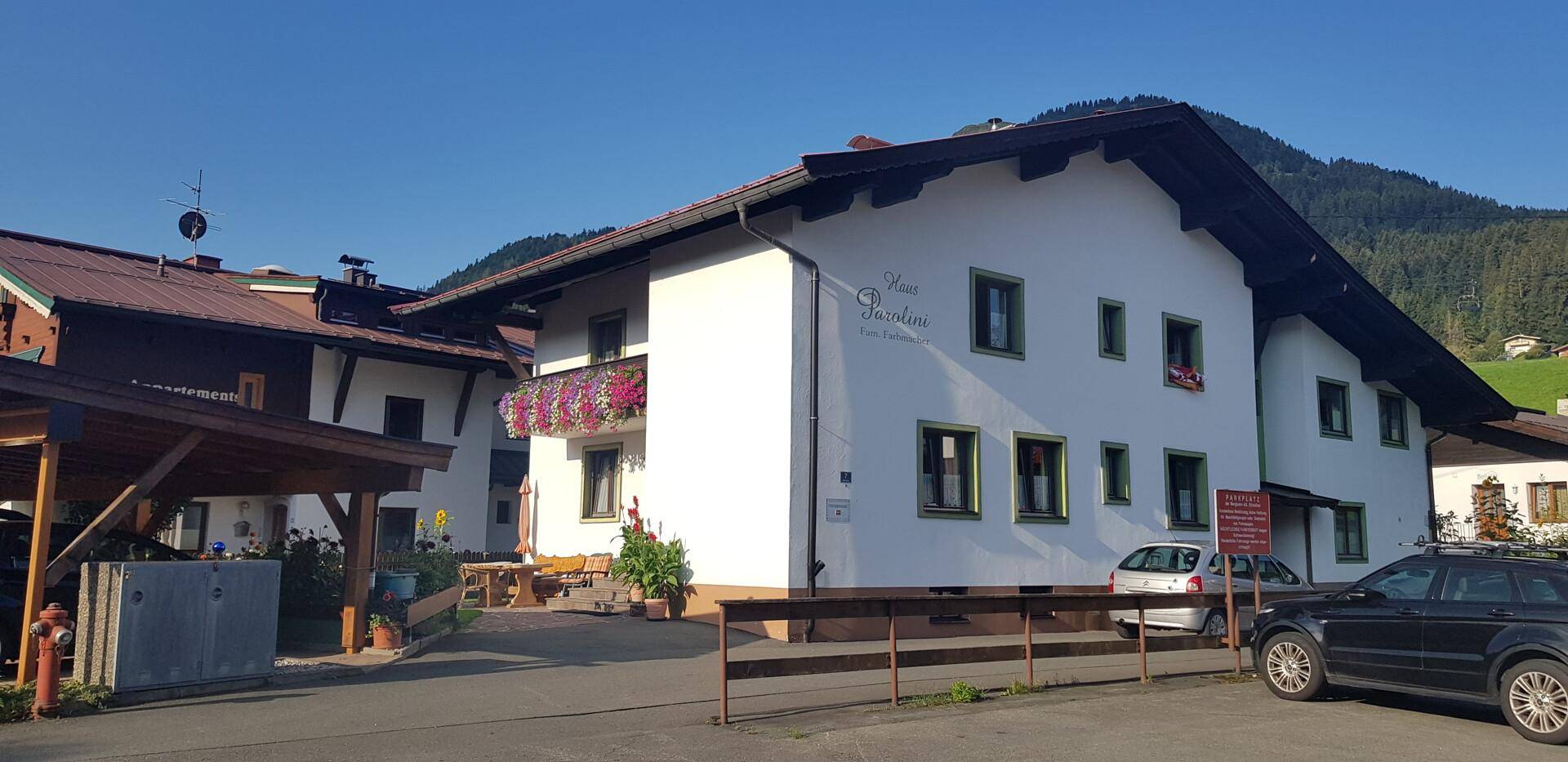 Alpines Gebäude mit weißer Fassade, Holzelementen und Carport in einer sonnigen Bergregion.