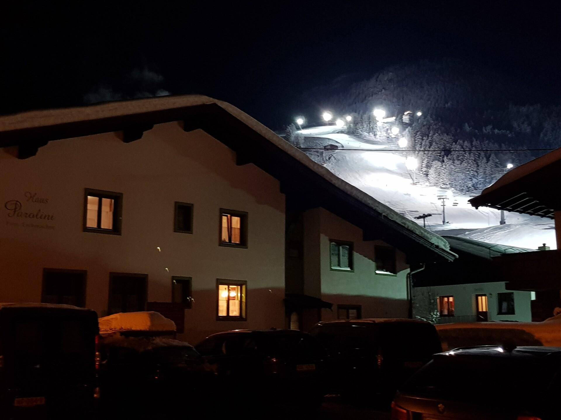 Alpines Gebäude bei Nacht mit beleuchteter Skipiste und verschneiter Landschaft im Hintergrund.