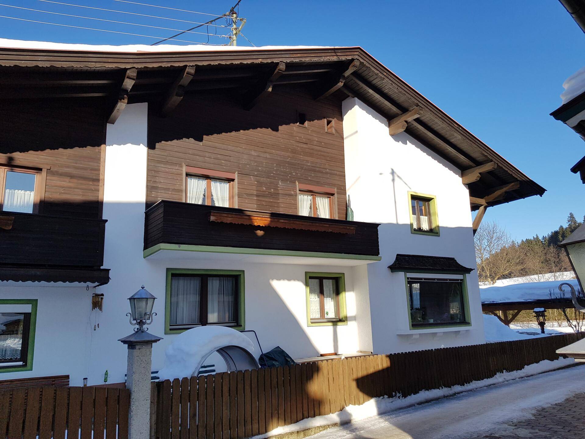 Alpines Gebäude mit Holzbalkonen und Schnee auf dem Dach und im Vorgarten im Winter.