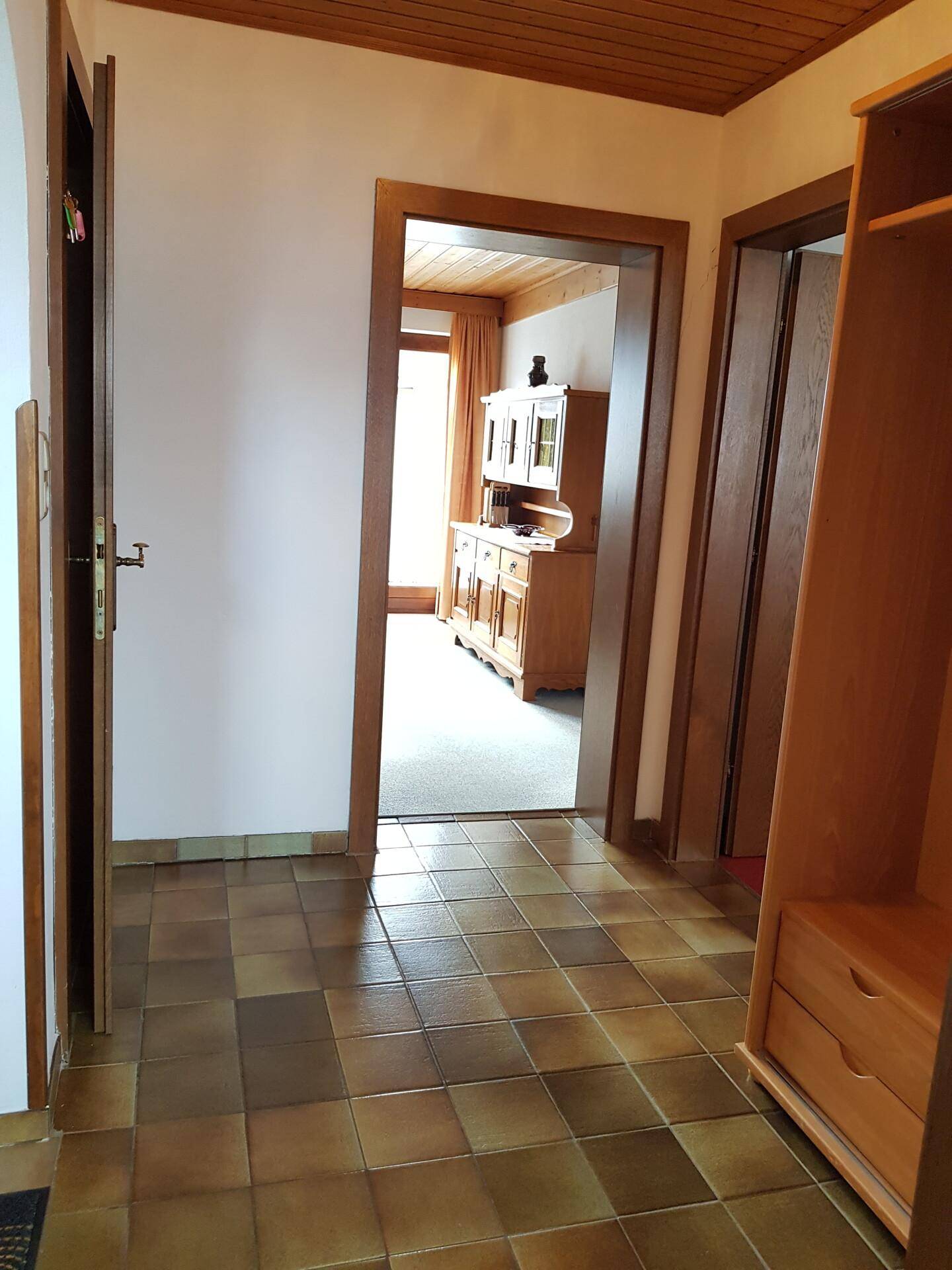 Eingangsbereich mit Fliesenboden und Holzmöbeln, der zu weiteren Räumen führt.