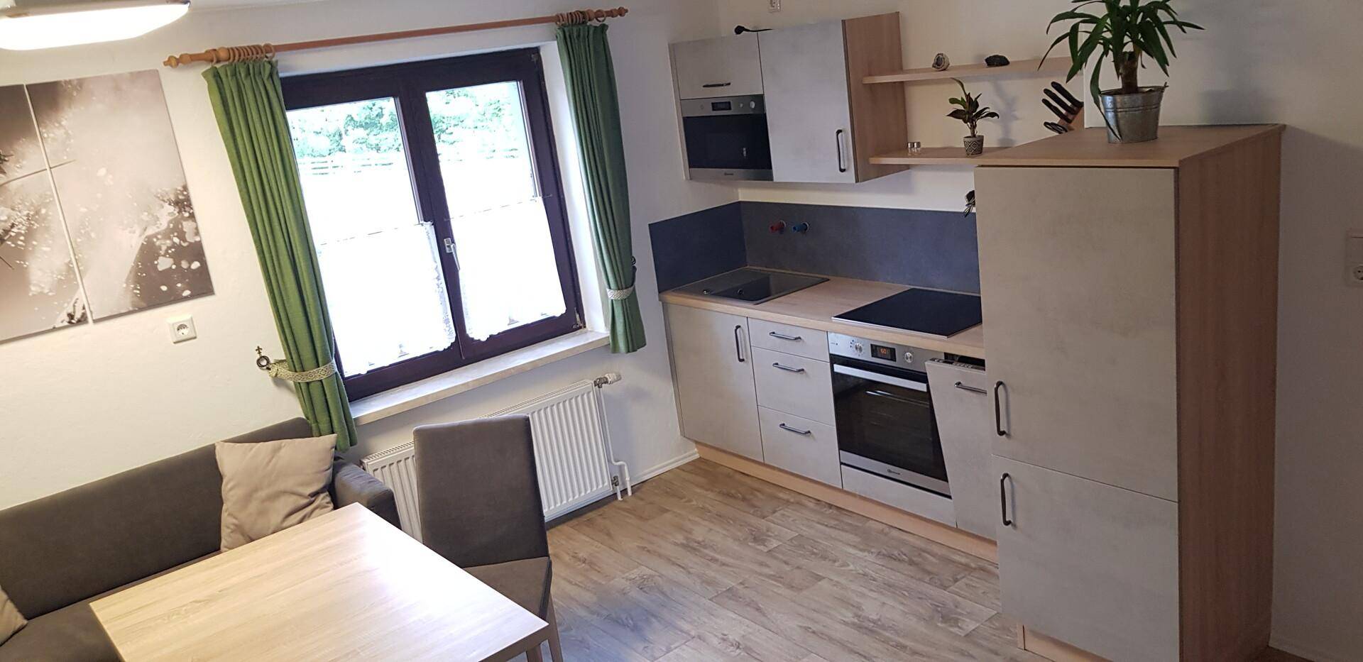 Kompakte Wohnküche mit moderner Einbauküche, Esstisch und Sofa in hellem Design.