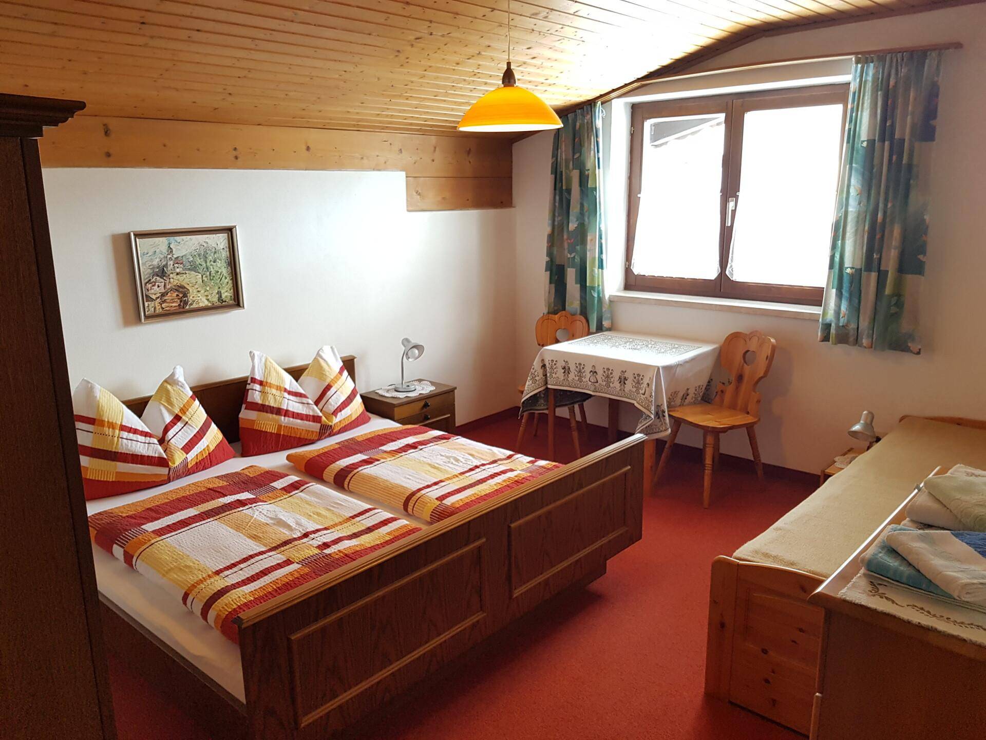 Schlafzimmer im alpinen Stil mit Holzdecke, Doppelbett und zusätzlichem Einzelbett.