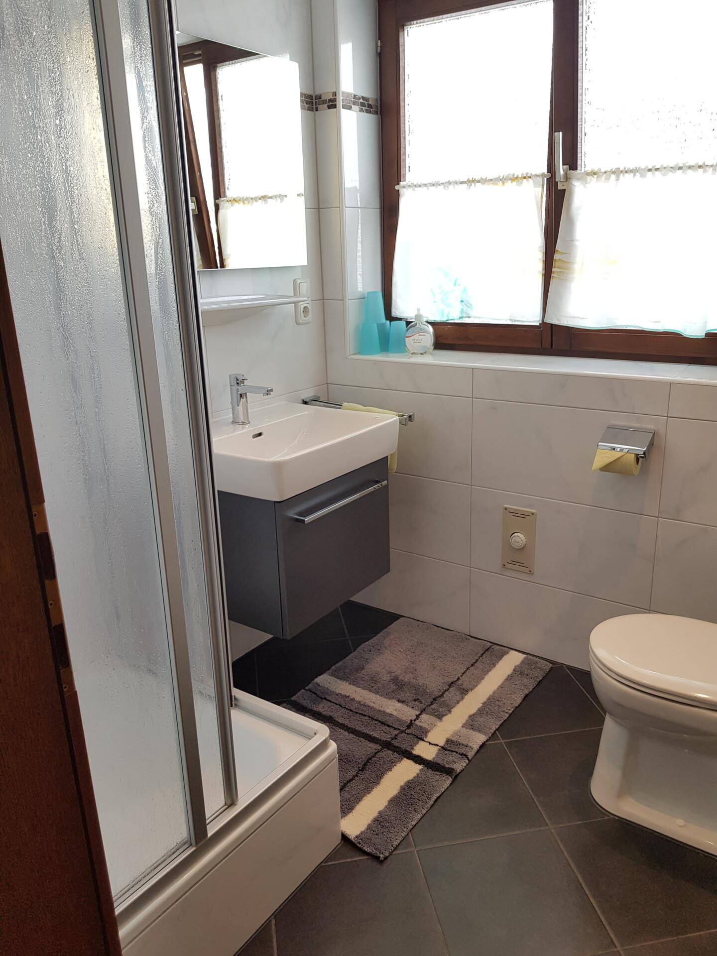 Modernes Badezimmer mit Dusche, Waschbecken und Fenster, hell gefliest.