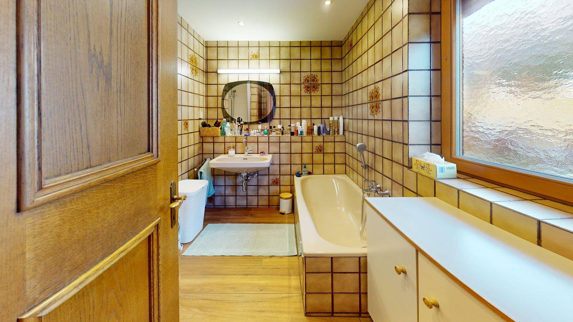 Badezimmer mit Badewanne, Waschbecken und Fliesen im 80er-Jahre-Stil.