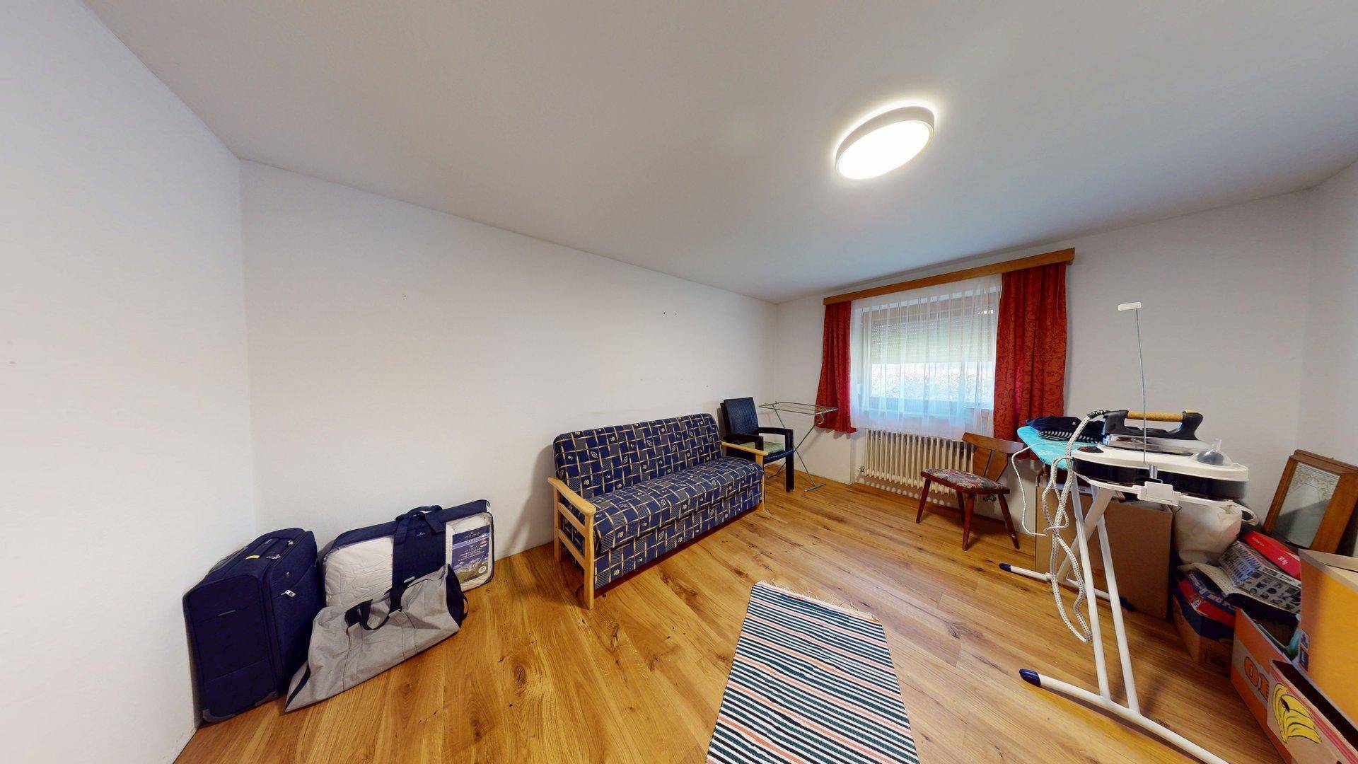 Flexibler Raum mit Holzboden, Schlafsofa und Fenster mit rotem Vorhang.