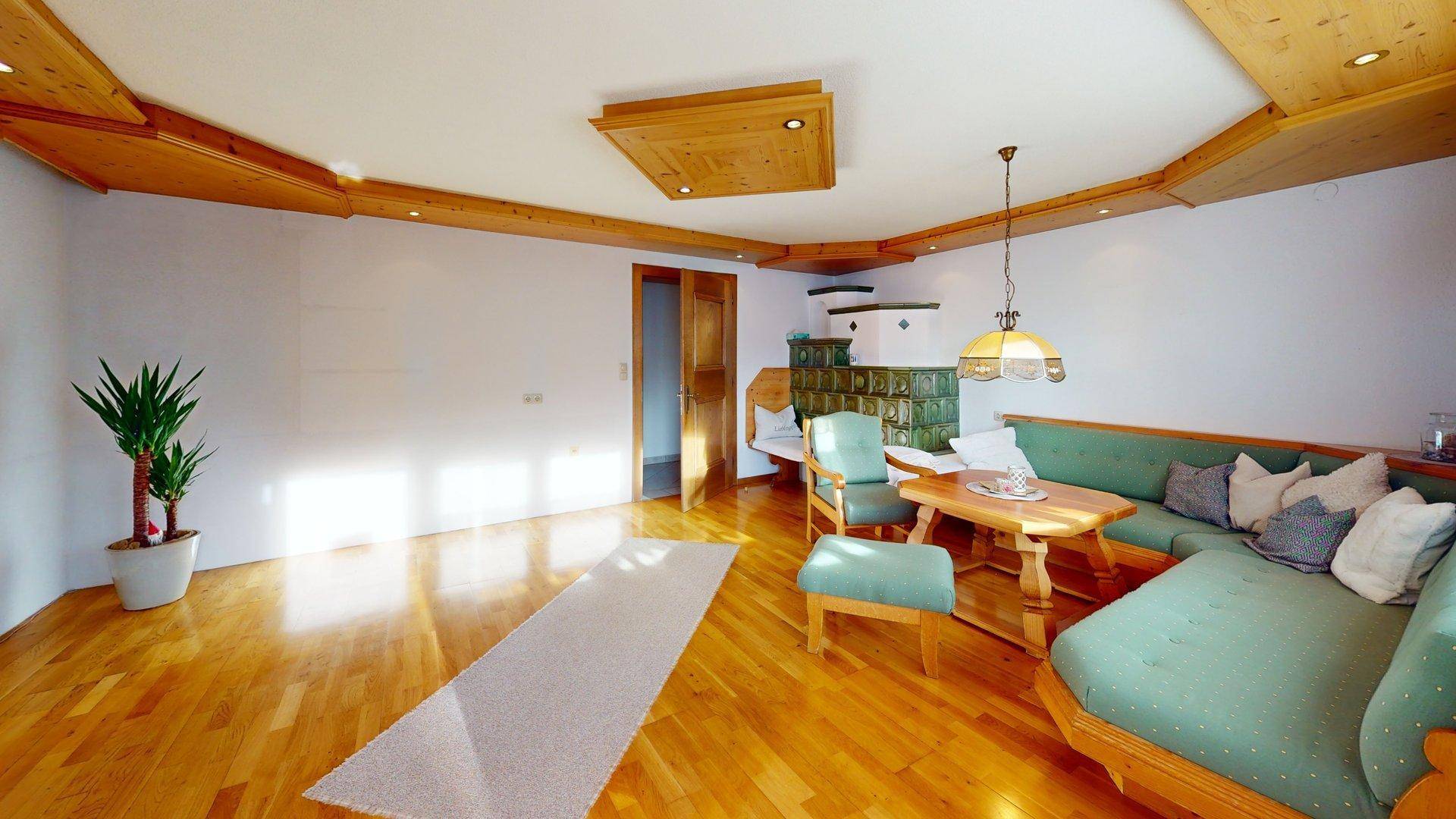 Geräumiges Wohnzimmer mit Holzboden, Kachelofen und traditioneller Holzeinrichtung.