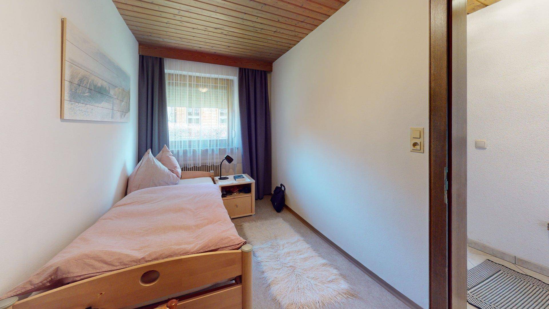 Kleines Schlafzimmer mit Einzelbett, Holzboden und Holzdecke.