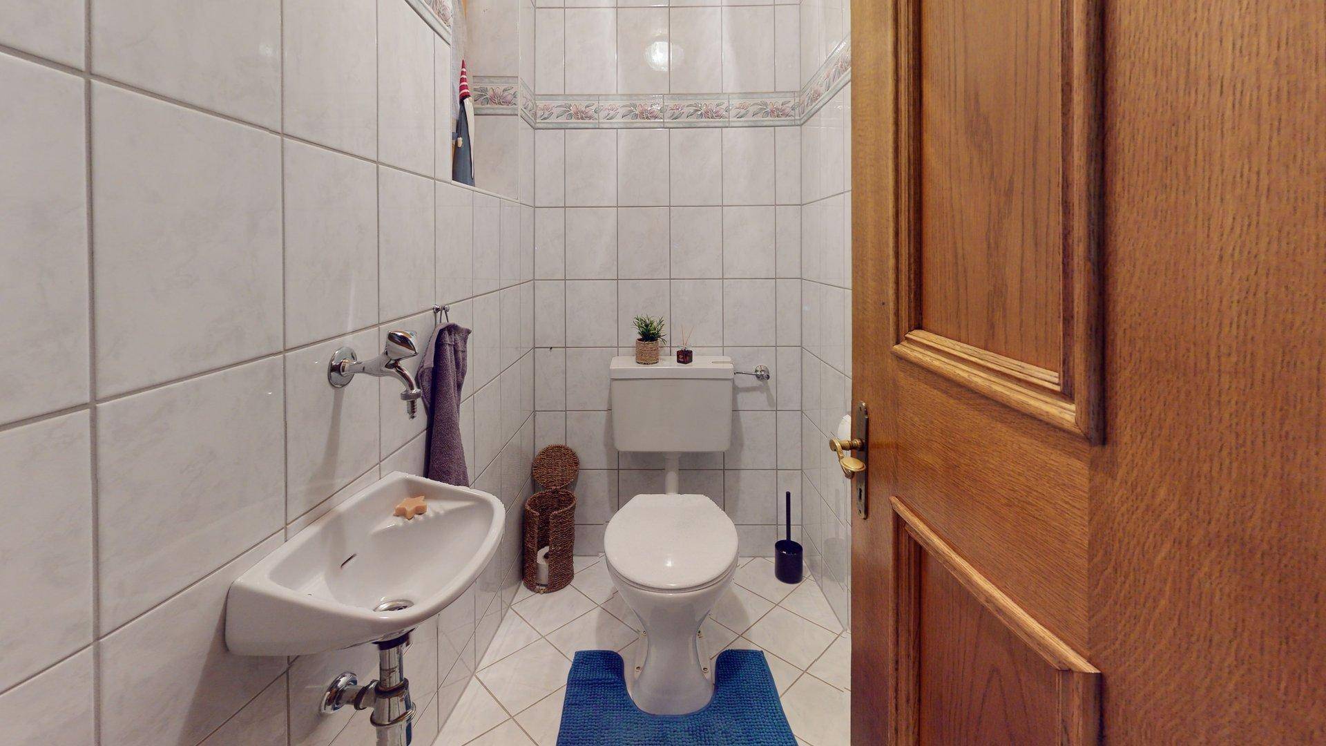 Kleines Gäste-WC mit weißem Fliesenboden und Wandwaschbecken.