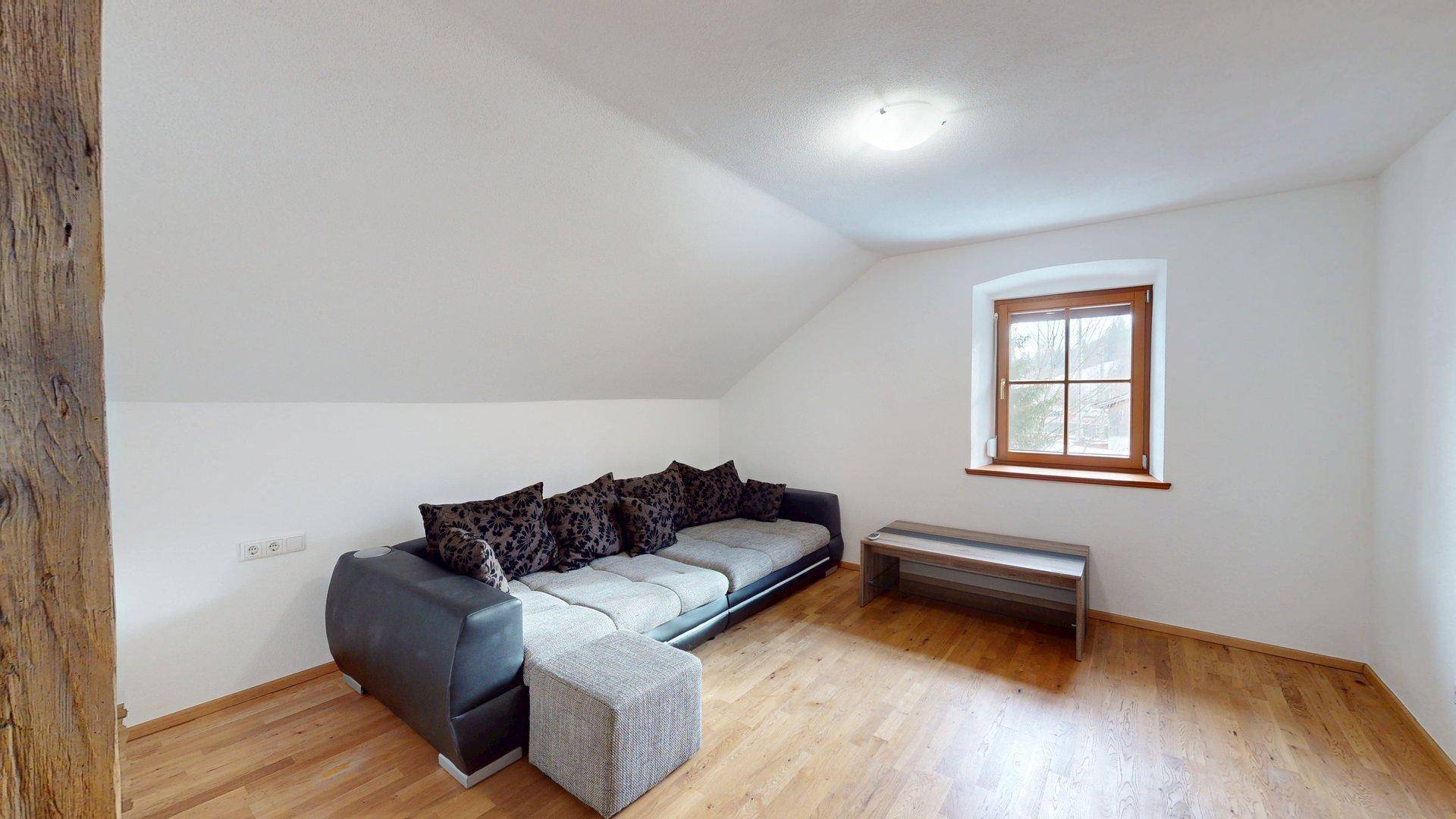 Geräumiges Wohnzimmer mit Sofa, Holzboden und Dachschräge, bietet viel Platz.