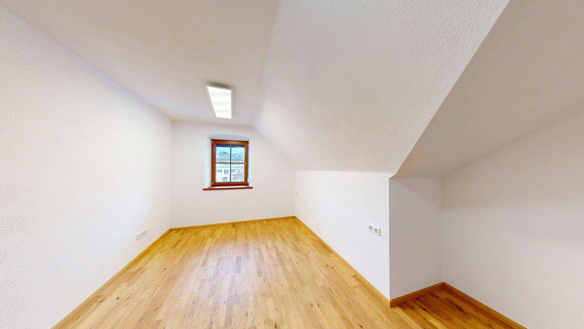 Leerer Raum mit Holzboden, weiß gestrichenen Wänden und Dachschräge.