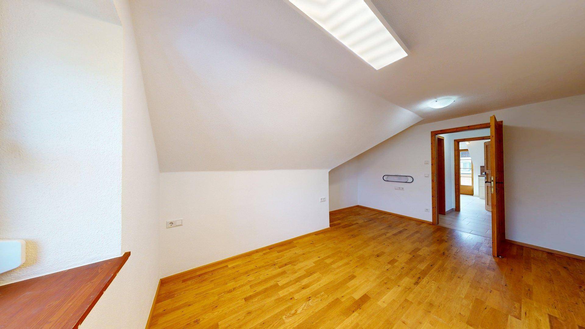 Heller Raum mit Holzboden, Dachschräge und Zugang zu weiteren Zimmern.