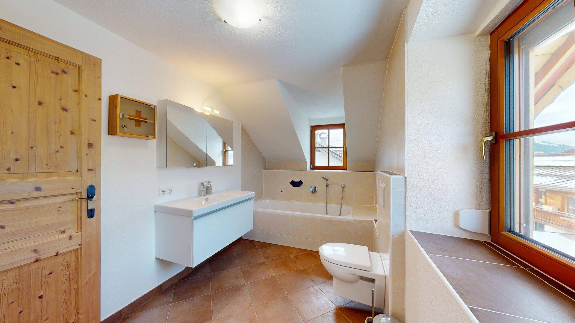 Modernes Badezimmer mit Badewanne, wandhängendem WC, Waschtisch und Fenster unter Dachschräge.