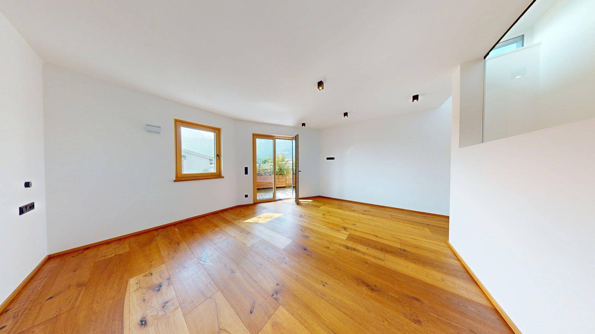 Heller Wohnbereich mit Holzboden, Balkonzugang und moderner Glasbrüstung.