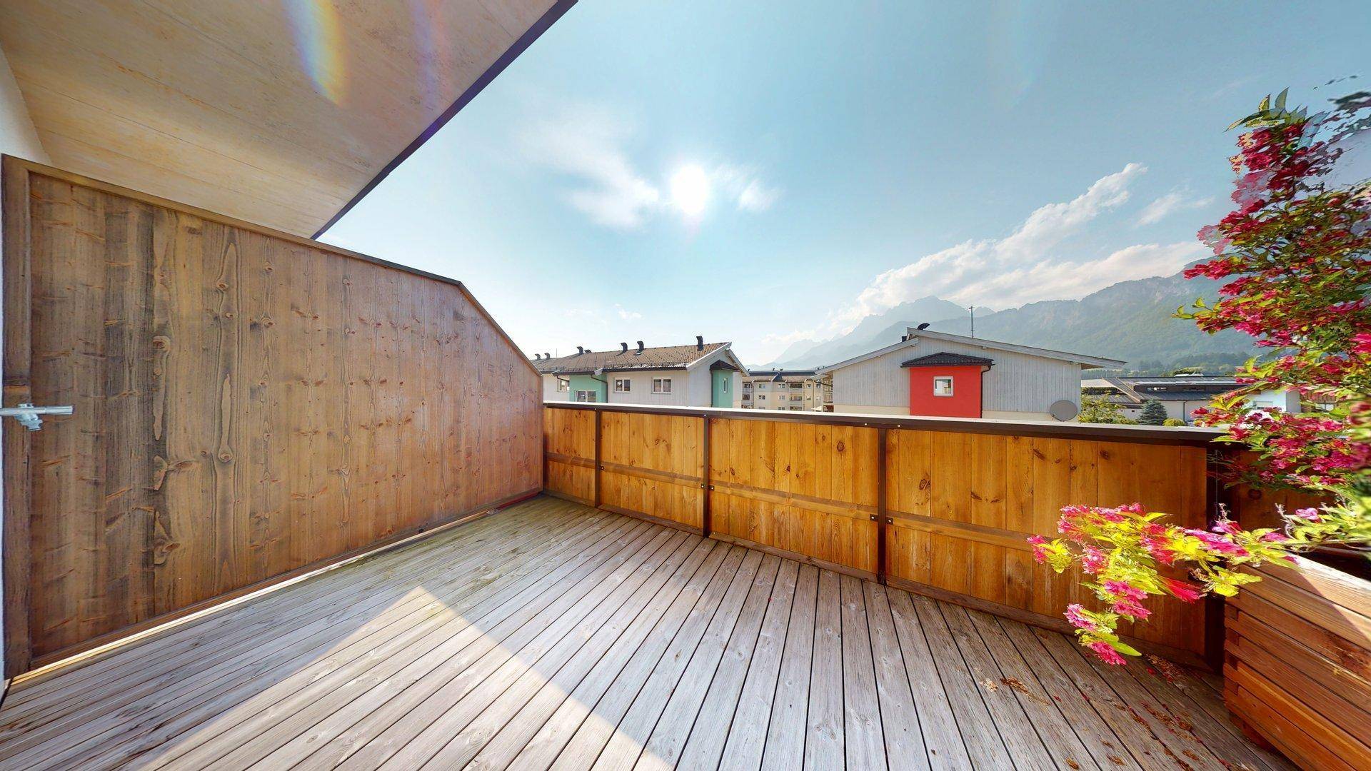 Sonniger Balkon mit Holzboden, Sichtschutz und malerischem Bergblick.
