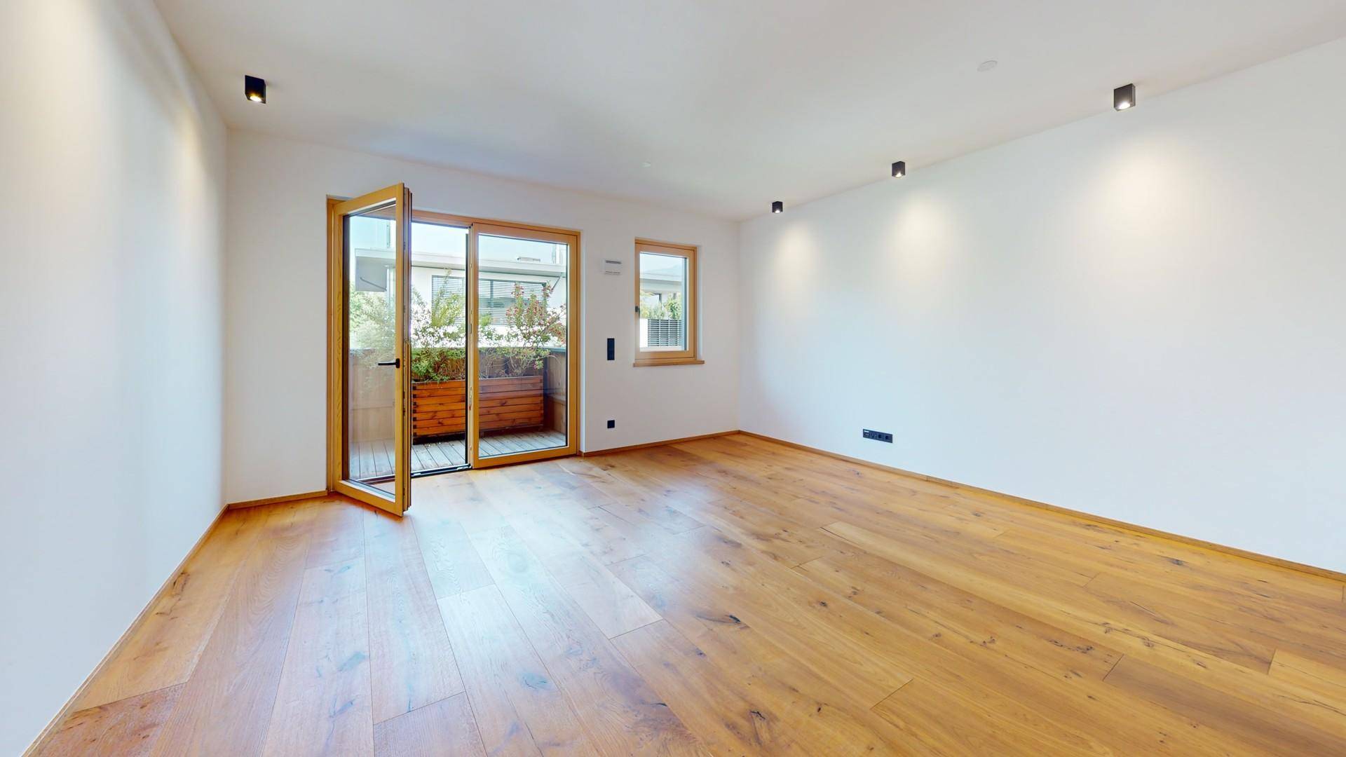 Helles Zimmer mit Holzboden und Zugang zu einem Balkon, ausgestattet mit modernen Deckenspots.