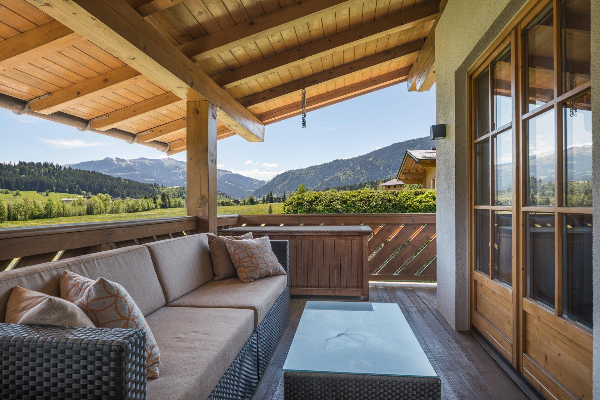 Gemütlicher Balkon mit Loungemöbeln und weitem Blick über die grüne Landschaft und Berge.