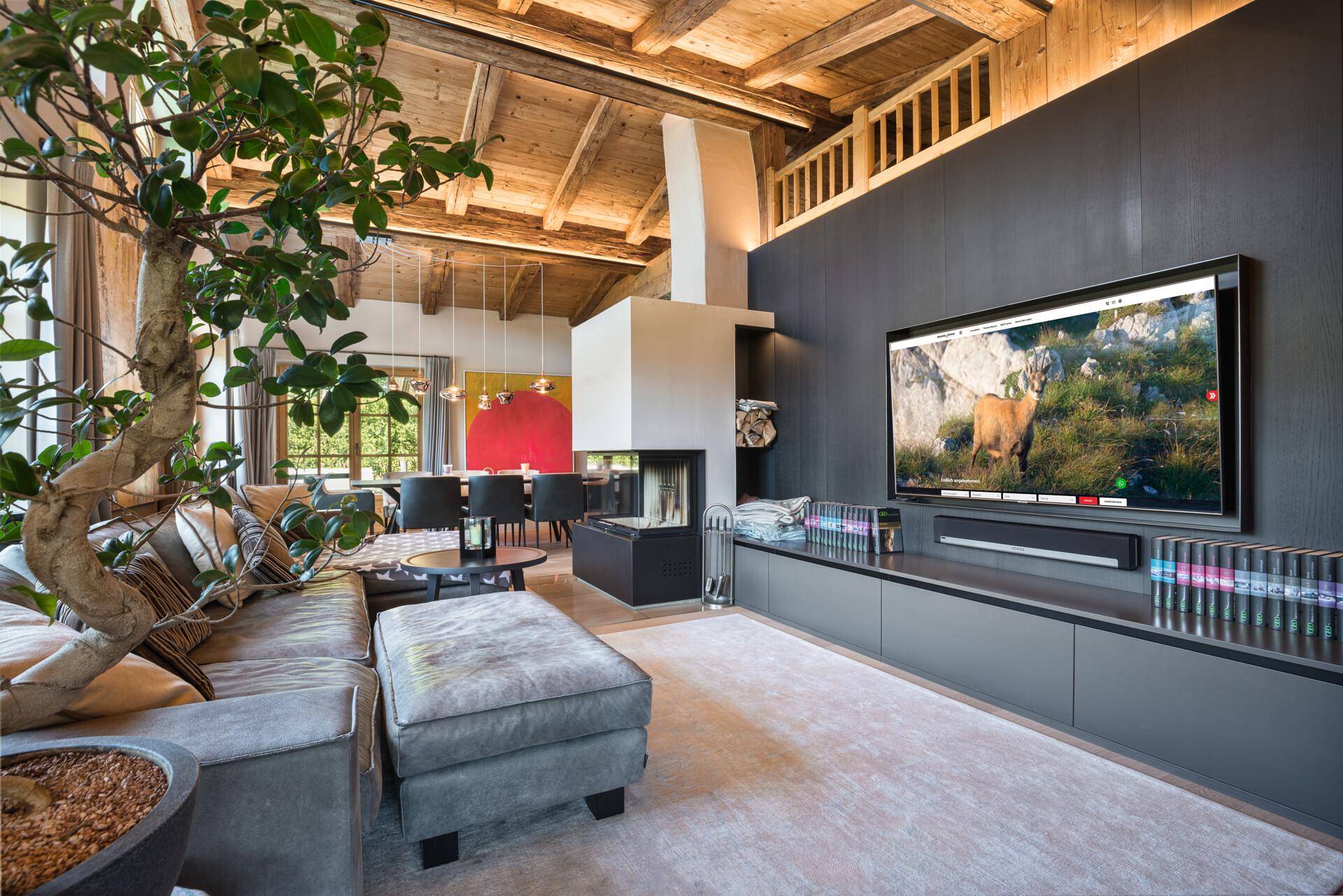Geräumiges Wohnzimmer mit Holzbalkendecke, Kamin und großem Fernseher, offen zum Essbereich.