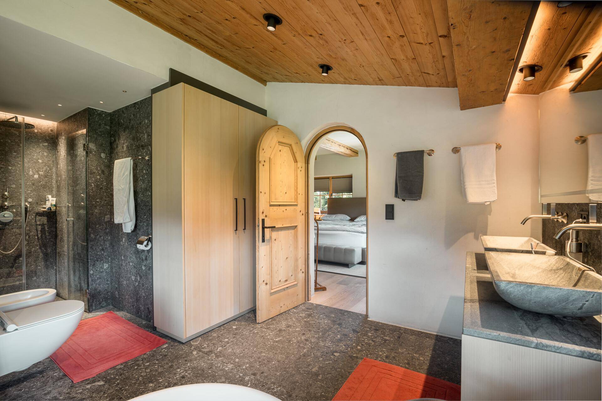 Modernes Badezimmer mit begehbarer Dusche, Bidet und Holztür zum Schlafzimmer.