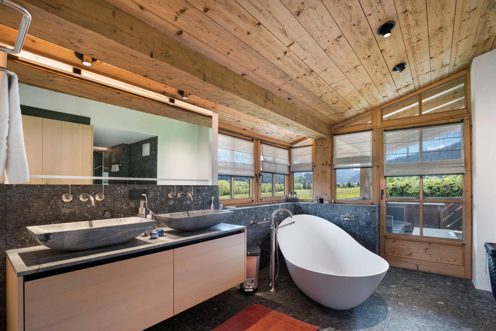 Luxuriöses Badezimmer mit freistehender Badewanne, Doppelwaschbecken und Holzbalkendecke.