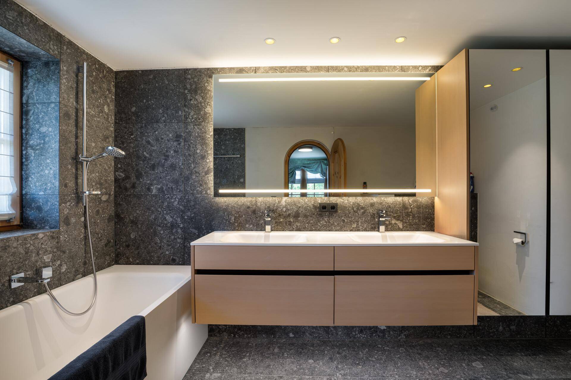 Modernes Badezimmer mit Badewanne, Doppelwaschbecken und beleuchtetem Spiegelschrank.