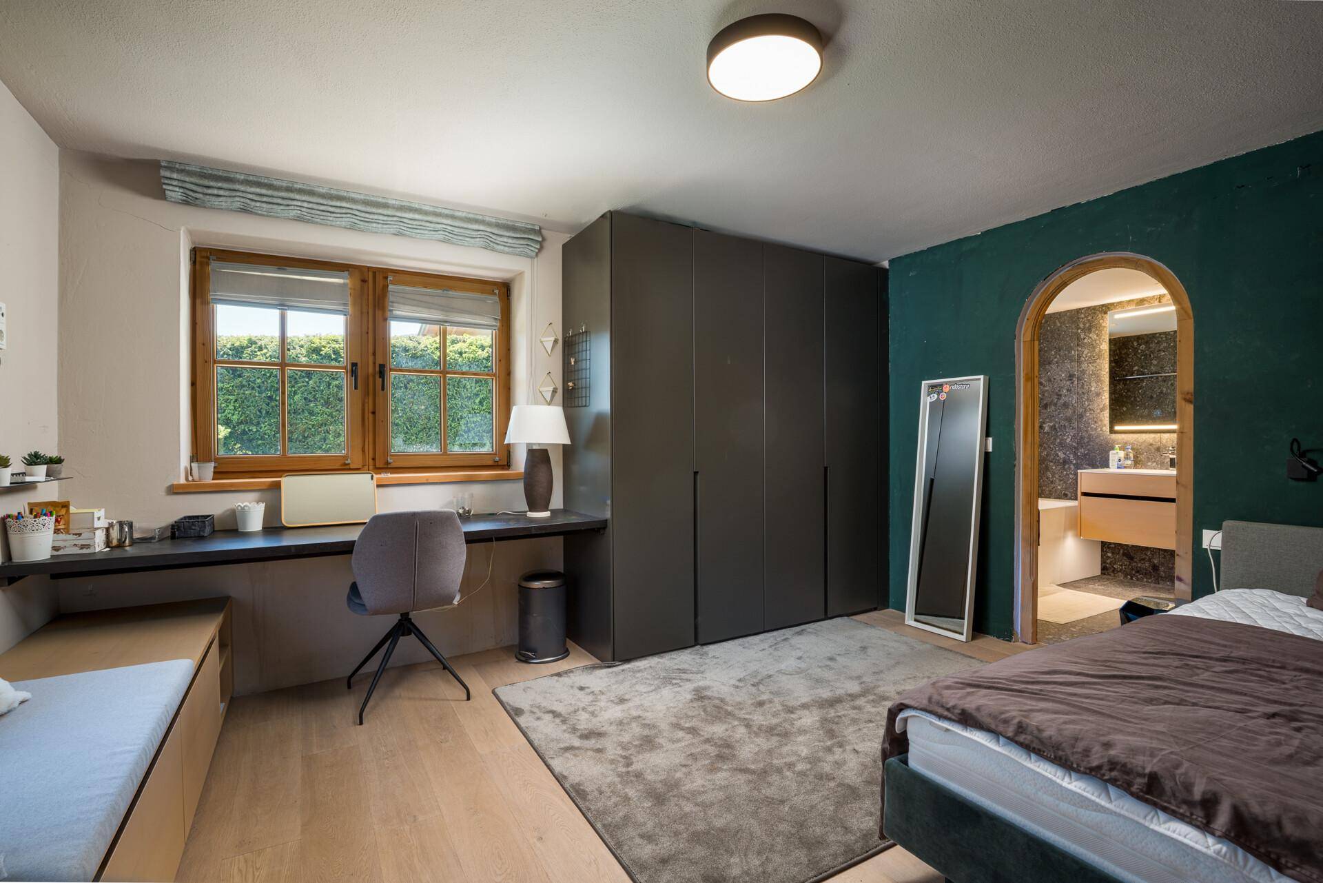 Schlafzimmer mit integriertem Schreibtisch, Einbauschränken und Zugang zu einem weiteren Bad.