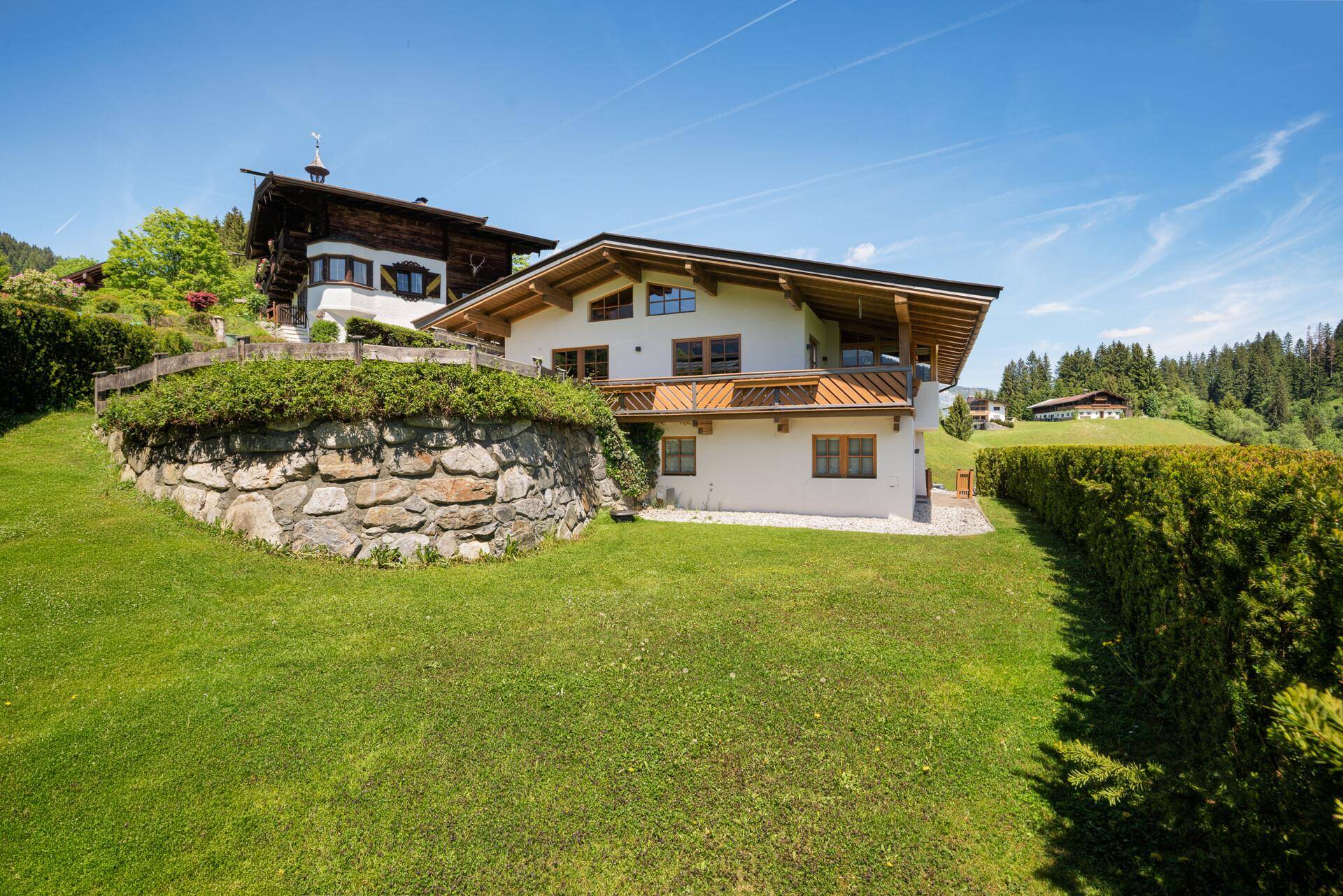Ansicht des Hauses mit gepflegtem Garten und Steinmauer in sonniger alpiner Umgebung.
