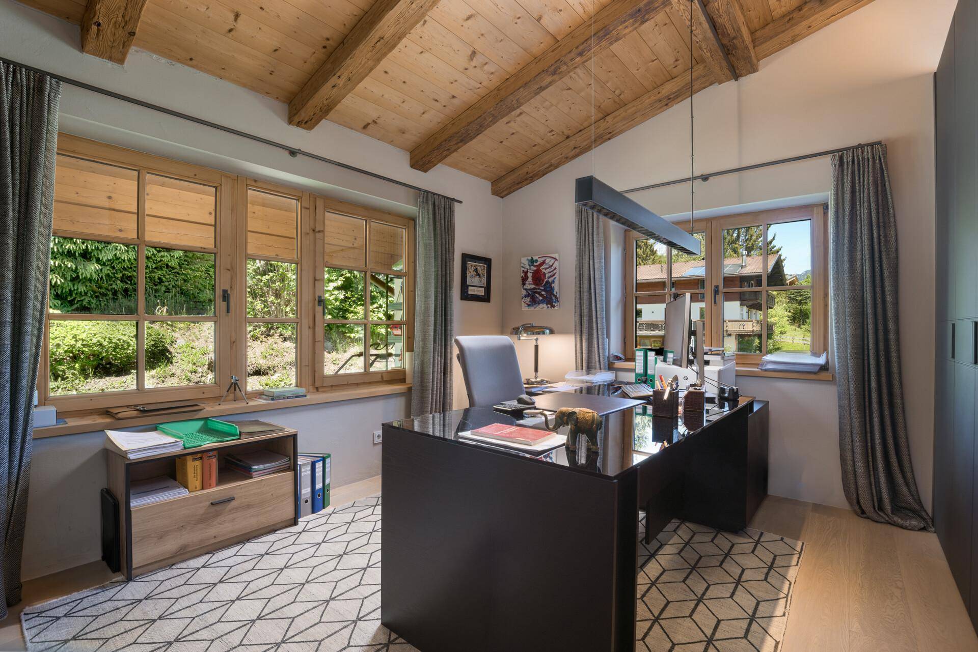Helles Arbeitszimmer mit Holzbalkendecke, großem Schreibtisch und Blick ins Grüne.