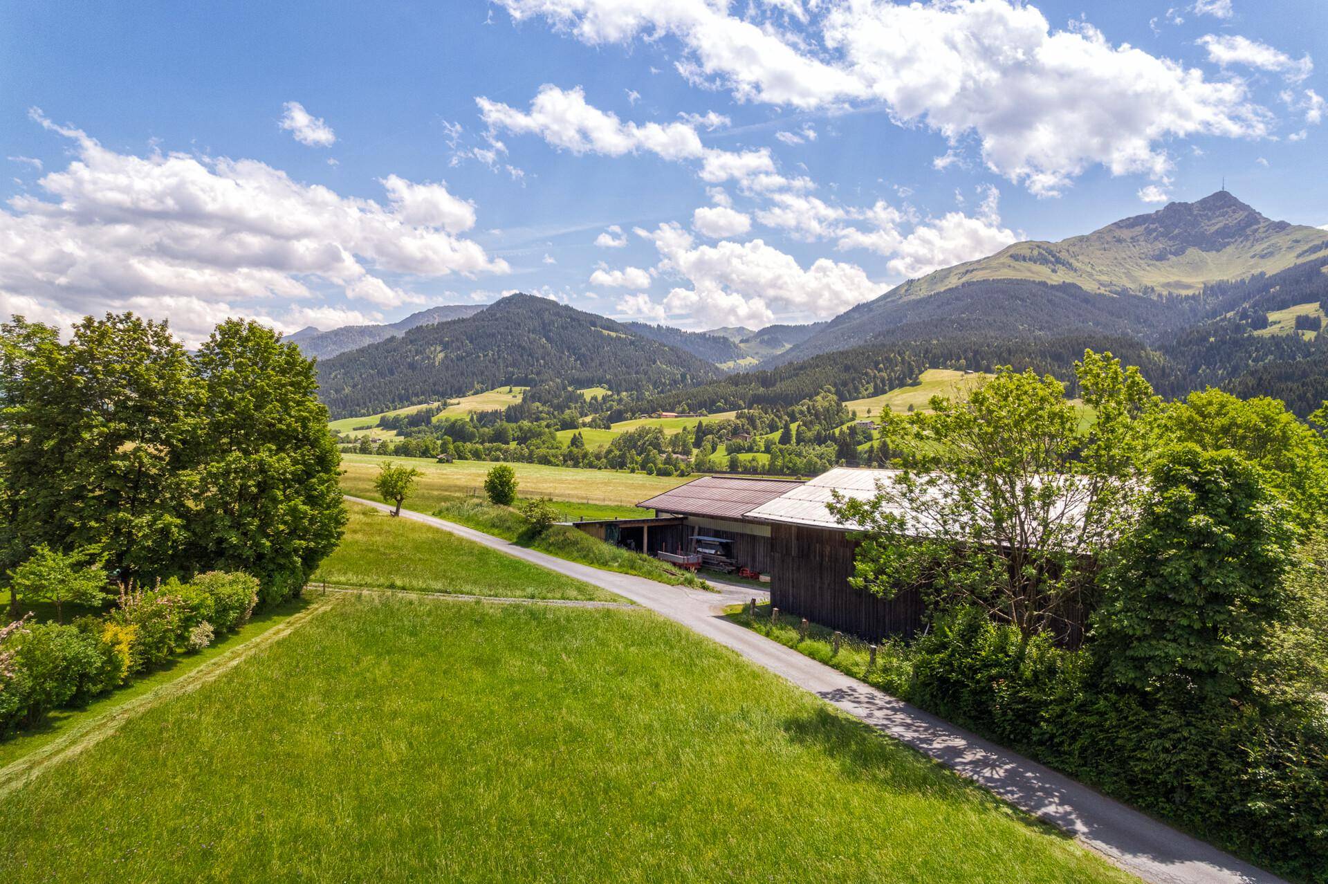 Panoramablick auf die sanften Hügel und Berge, umgeben von üppigem Grün und einem traditionellen Bauernhaus.