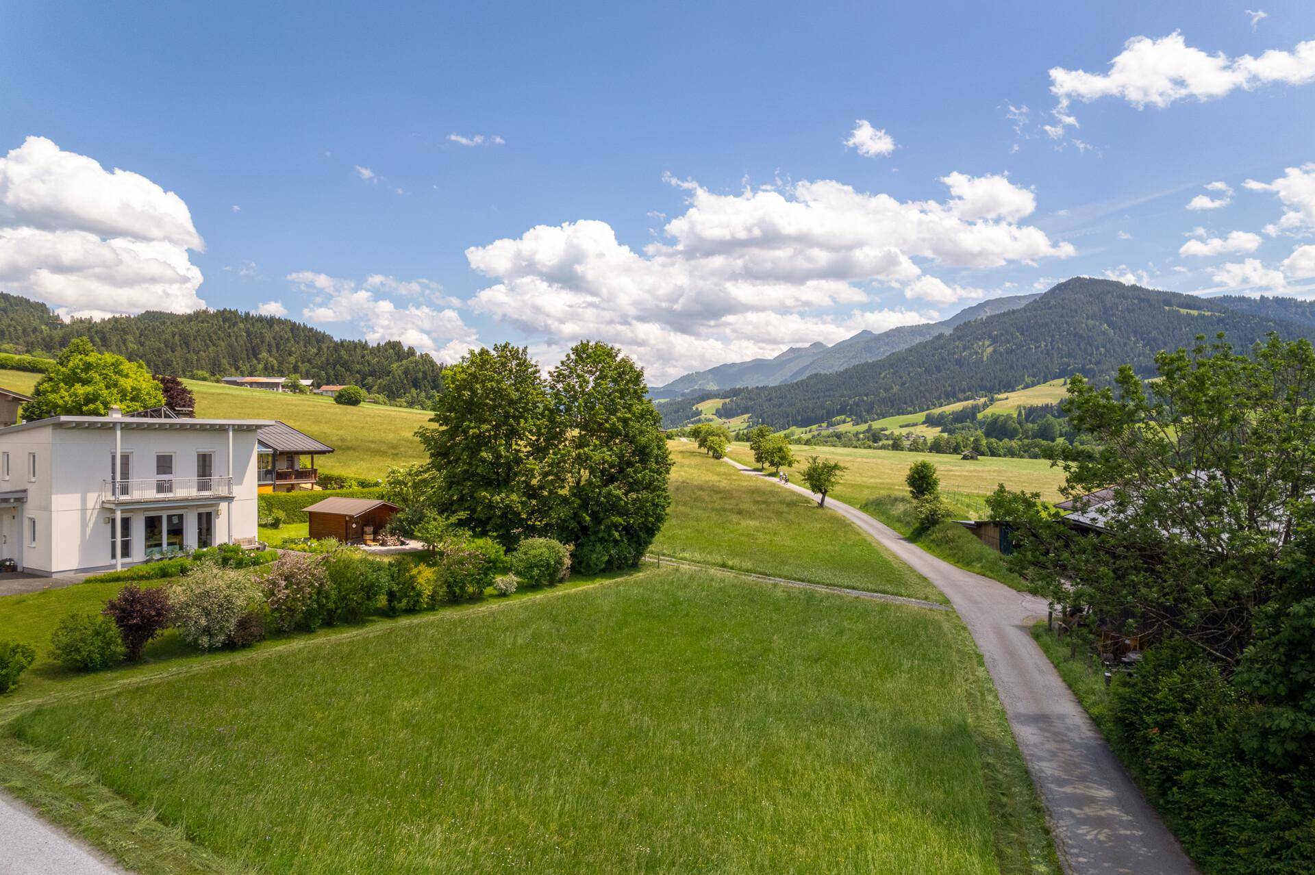 Weitläufige grüne Landschaft mit einem modernen Wohnhaus und einem atemberaubenden Blick auf die Alpen.