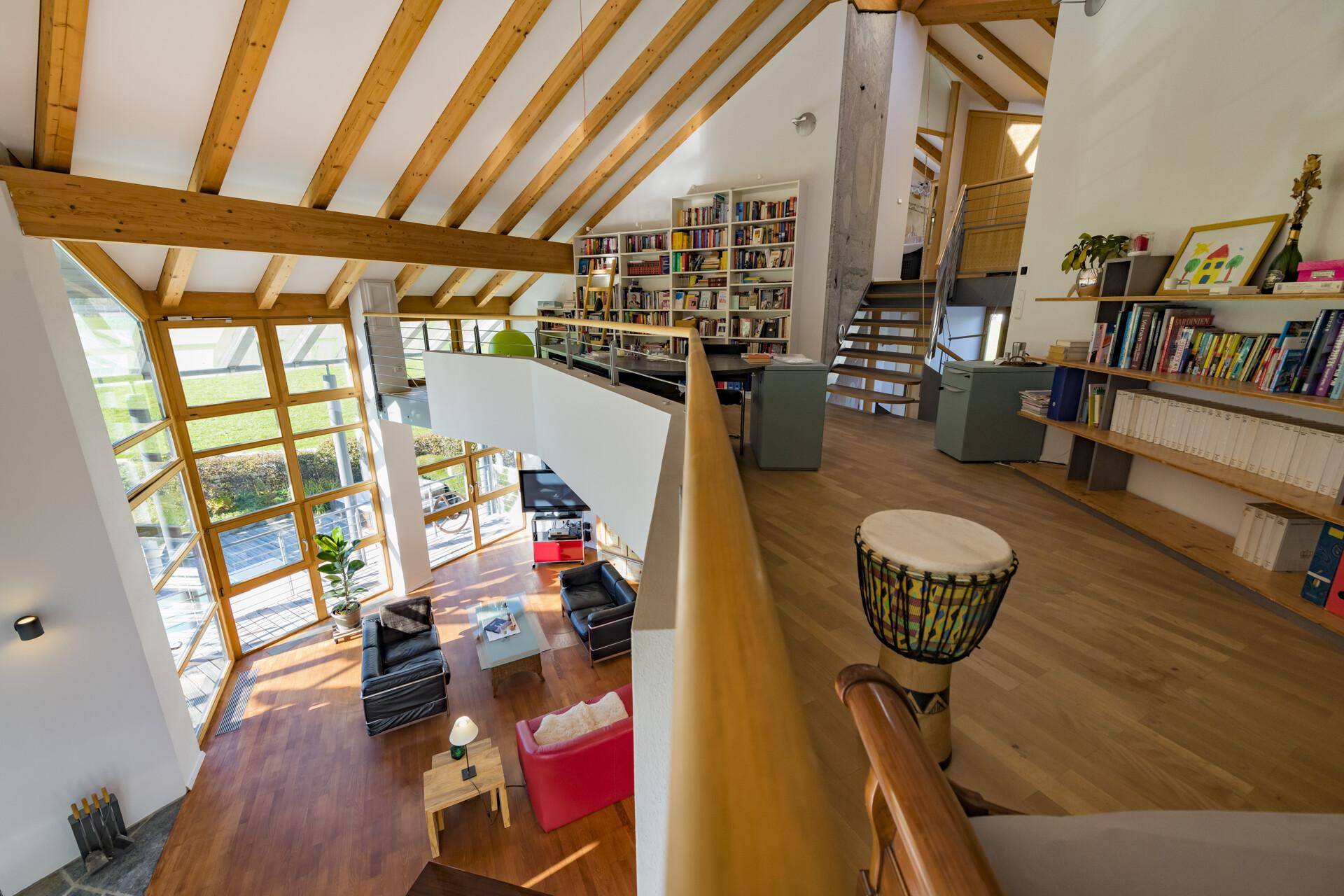 Blick von der Galerie auf den offenen Wohnbereich mit hohen Decken und großen Fenstern.