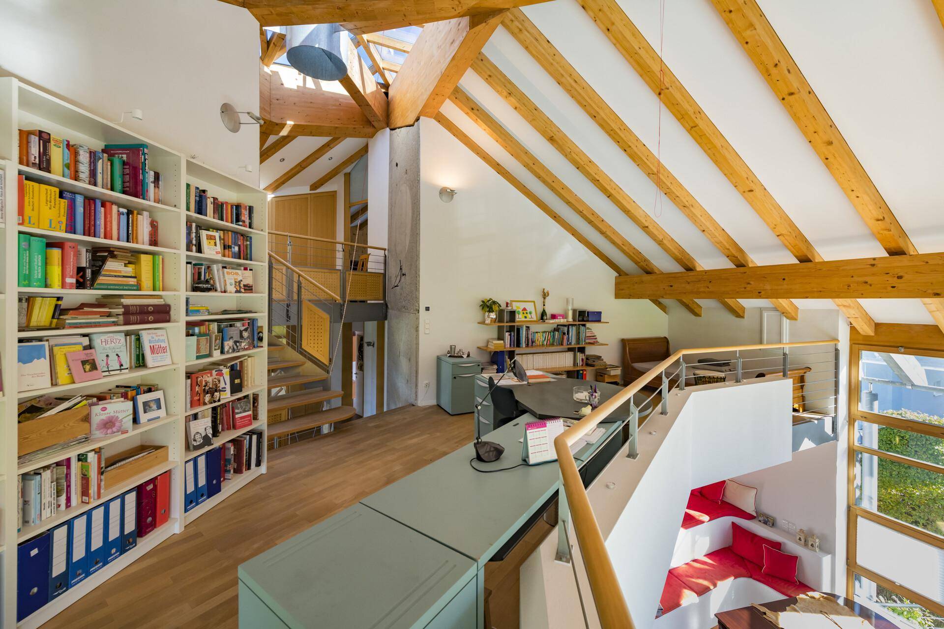 Geräumiger Arbeitsbereich mit Bücherregalen, Holzbalken und Blick auf den lichtdurchfluteten Wohnbereich.