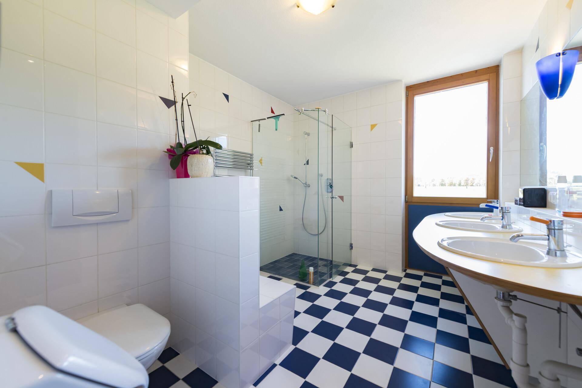 Modernes Badezimmer mit Dusche, Doppelwaschbecken und auffälligen blau-weißen Schachbrettfliesen.