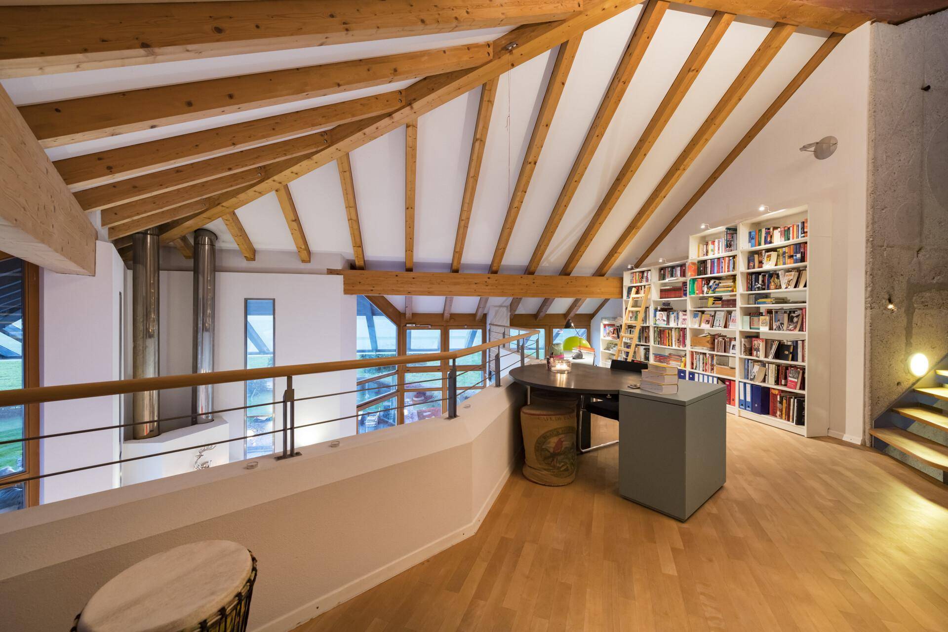 Offener Arbeitsbereich auf der Galerie mit Bücherregalen, Holzbalken und Blick in den Wohnbereich.