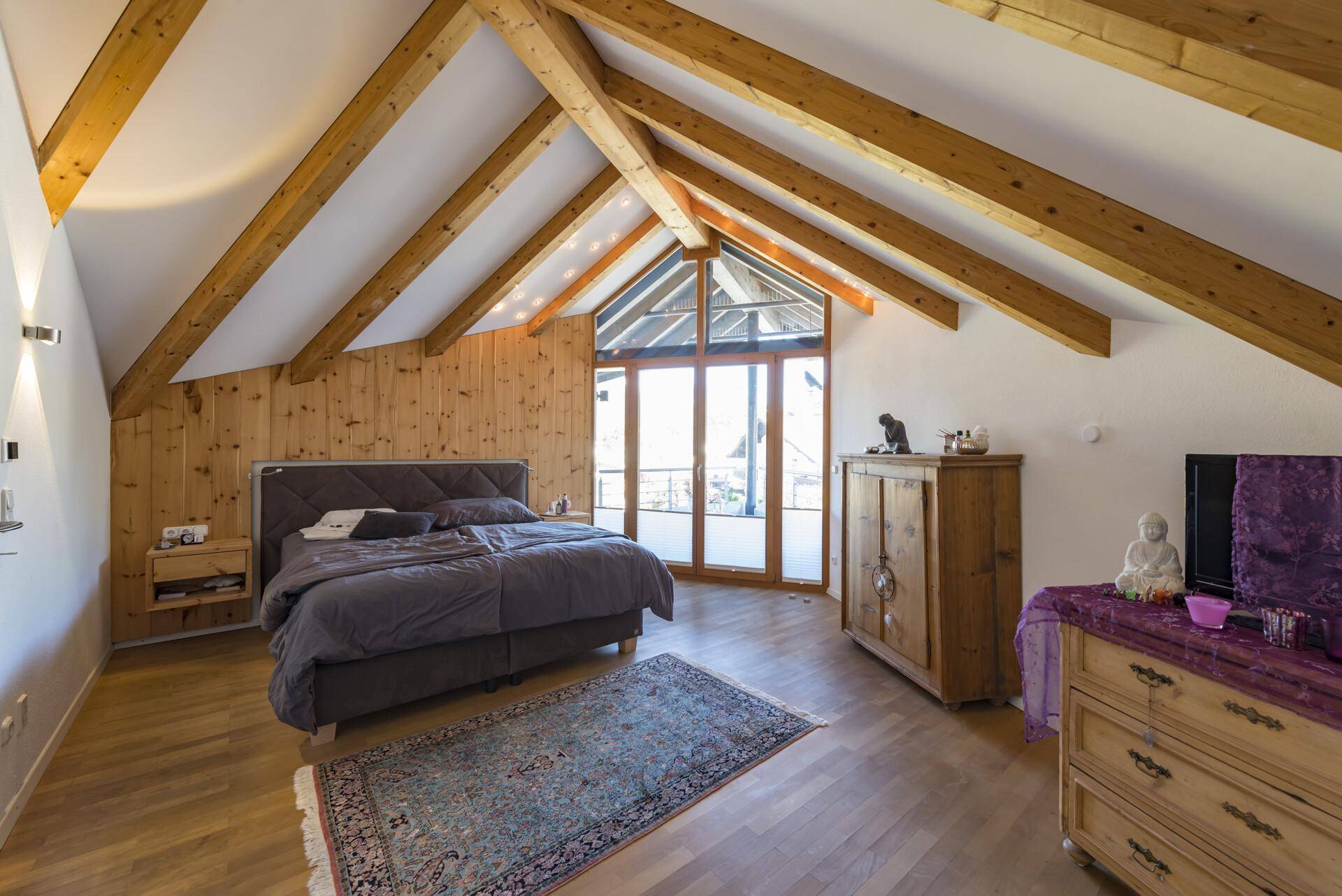 Gemütliches Schlafzimmer mit Holzbalken, Dachschräge und Zugang zu einem französischen Balkon.