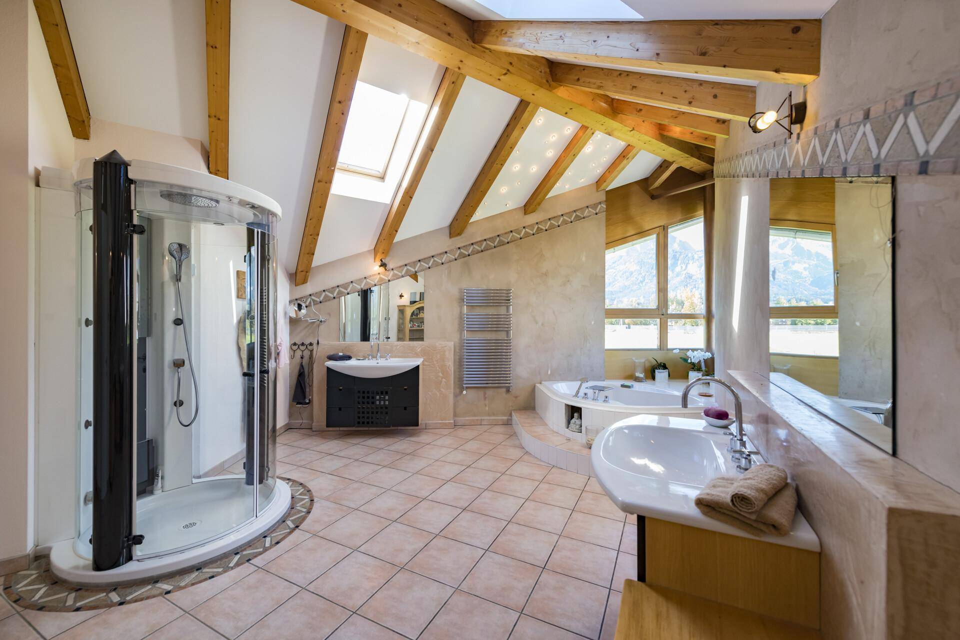 Großes Badezimmer mit Dusche, Badewanne, Doppelwaschbecken und Holzbalken unter der Dachschräge.