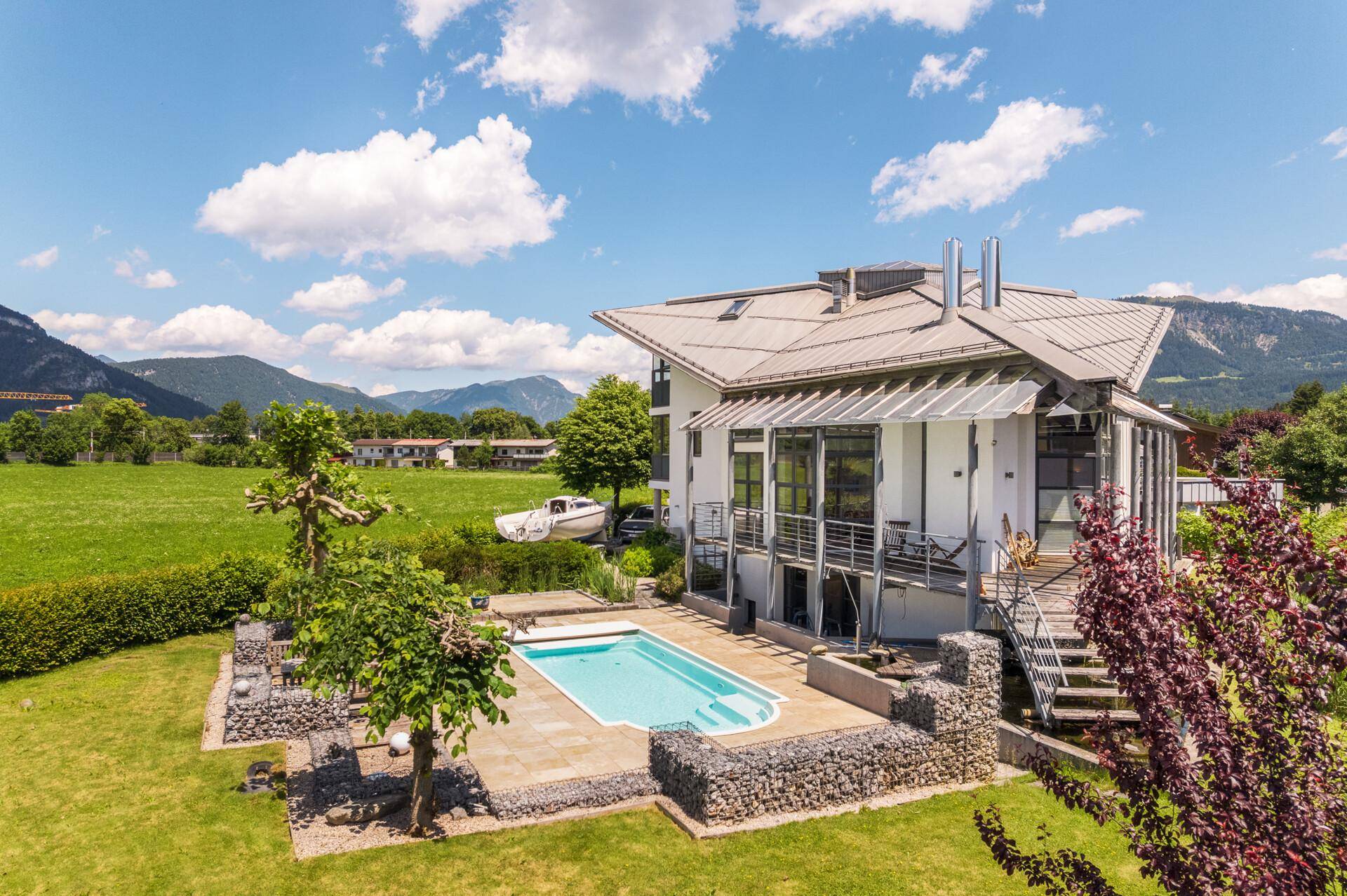 Luftaufnahme der modernen Villa mit Pool, großem Garten und malerischer Bergkulisse im Hintergrund.
