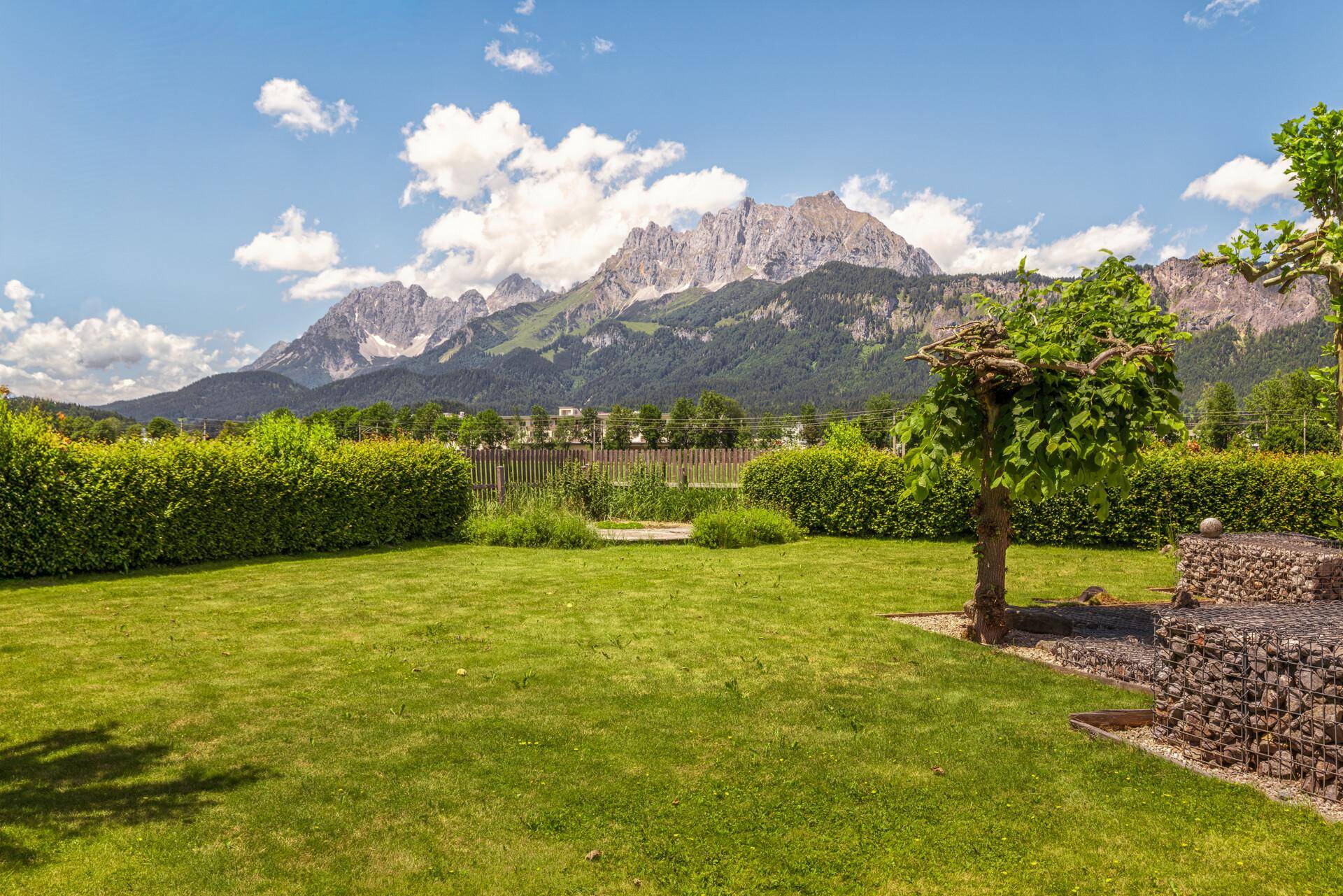 Gepflegter Garten mit Rasenfläche, Hecken und einem weiten Blick auf die majestätischen Berge.