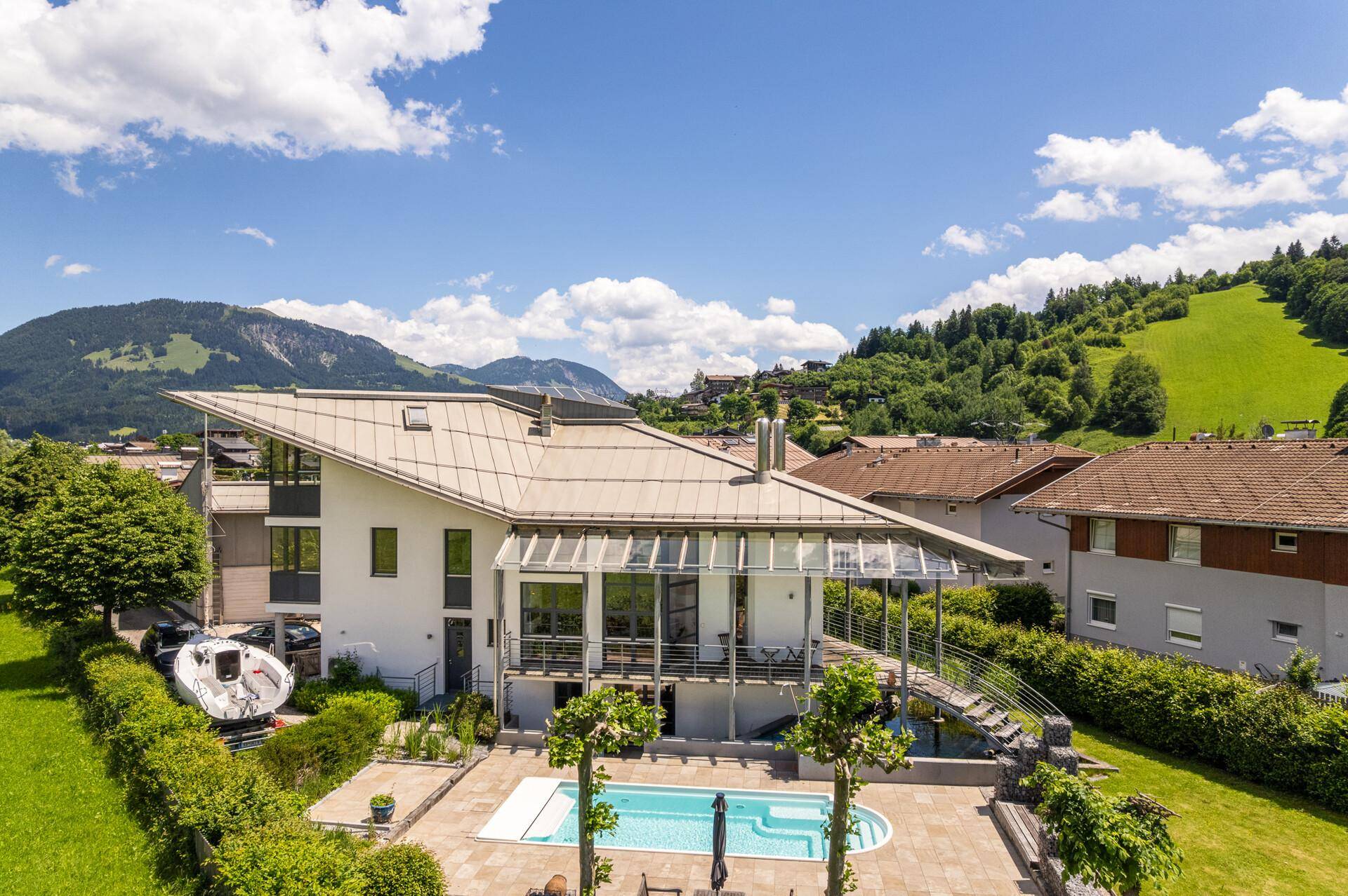 Luftaufnahme der modernen Villa mit Pool und Garten, eingebettet in eine grüne Berglandschaft.
