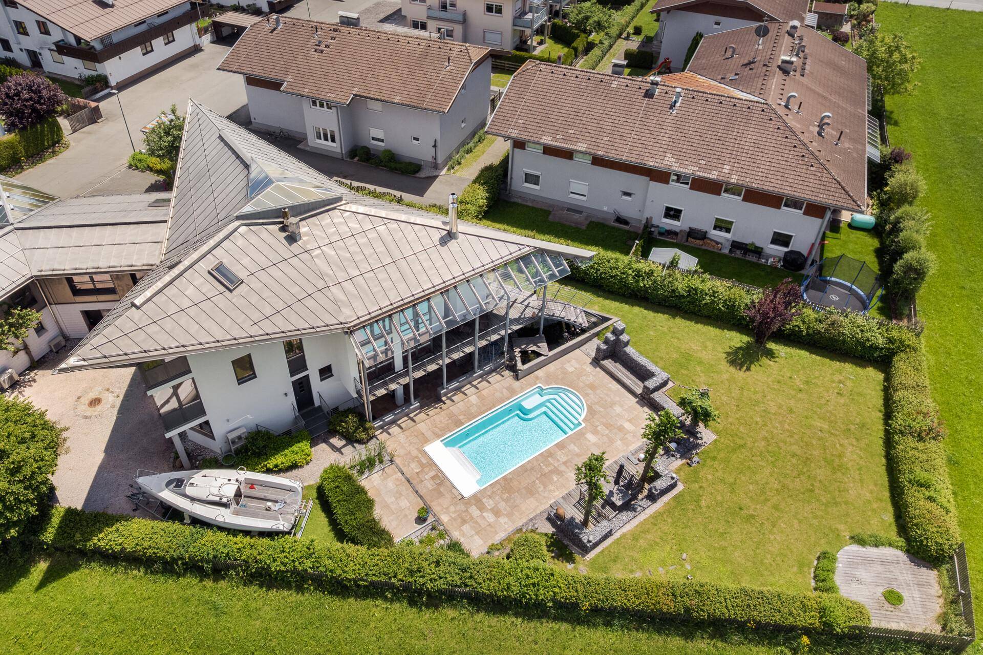 Luftaufnahme eines modernen Hauses mit großem Garten, Pool und umliegender Wohnbebauung.