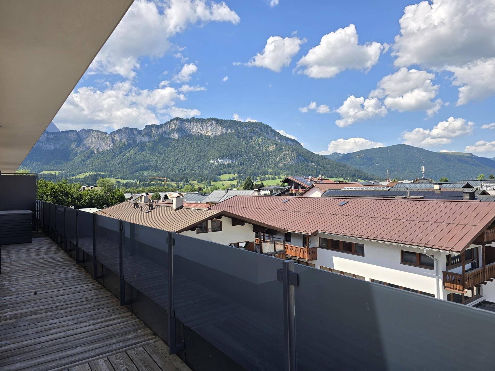 Geräumige Terrasse mit Holzboden und Panoramablick auf die grünen Berge und die Dächer der Stadt.