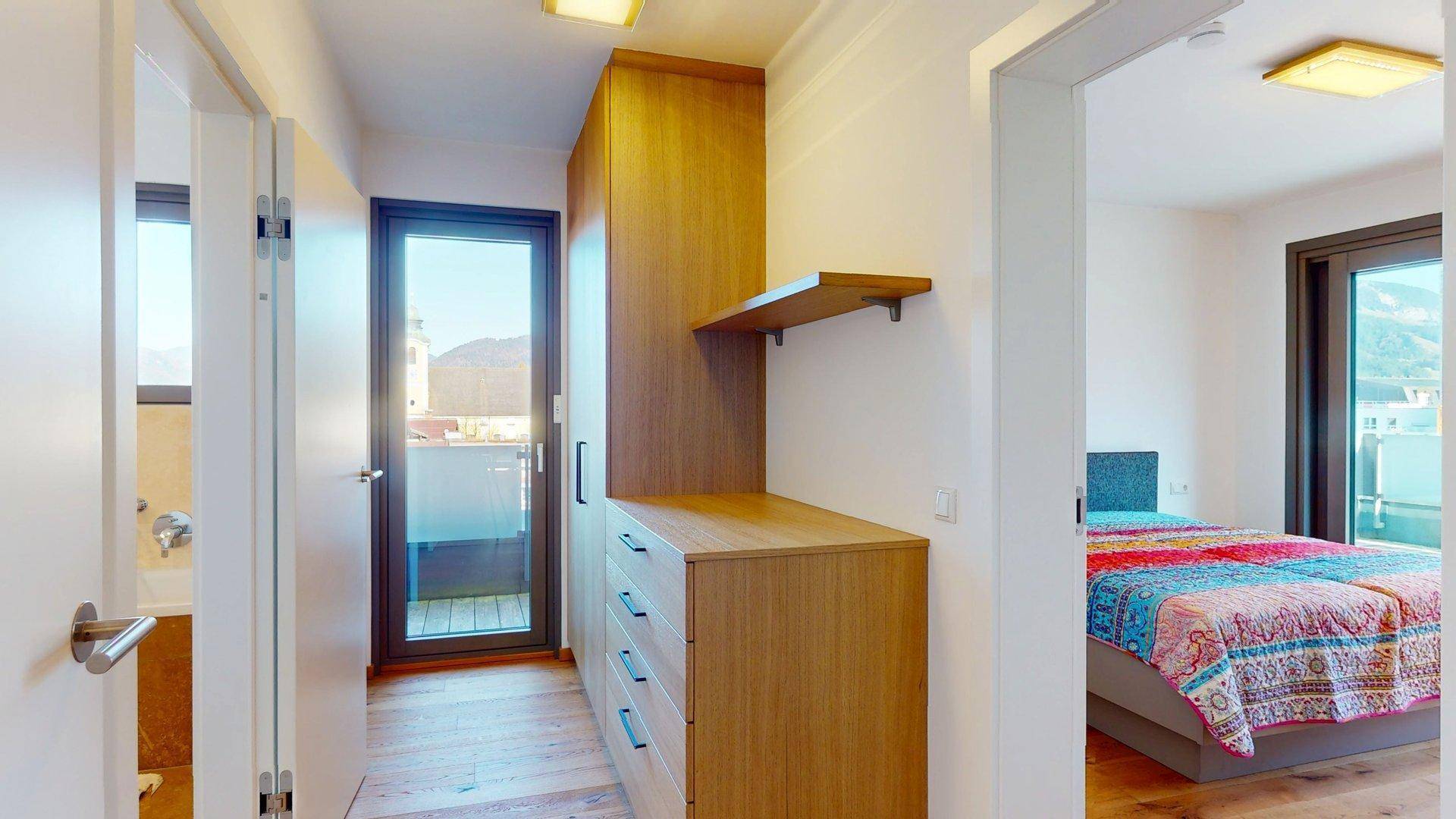 Flur mit Einbauschränken, Holzboden und Zugang zum Schlafzimmer und zur Außenterrasse.