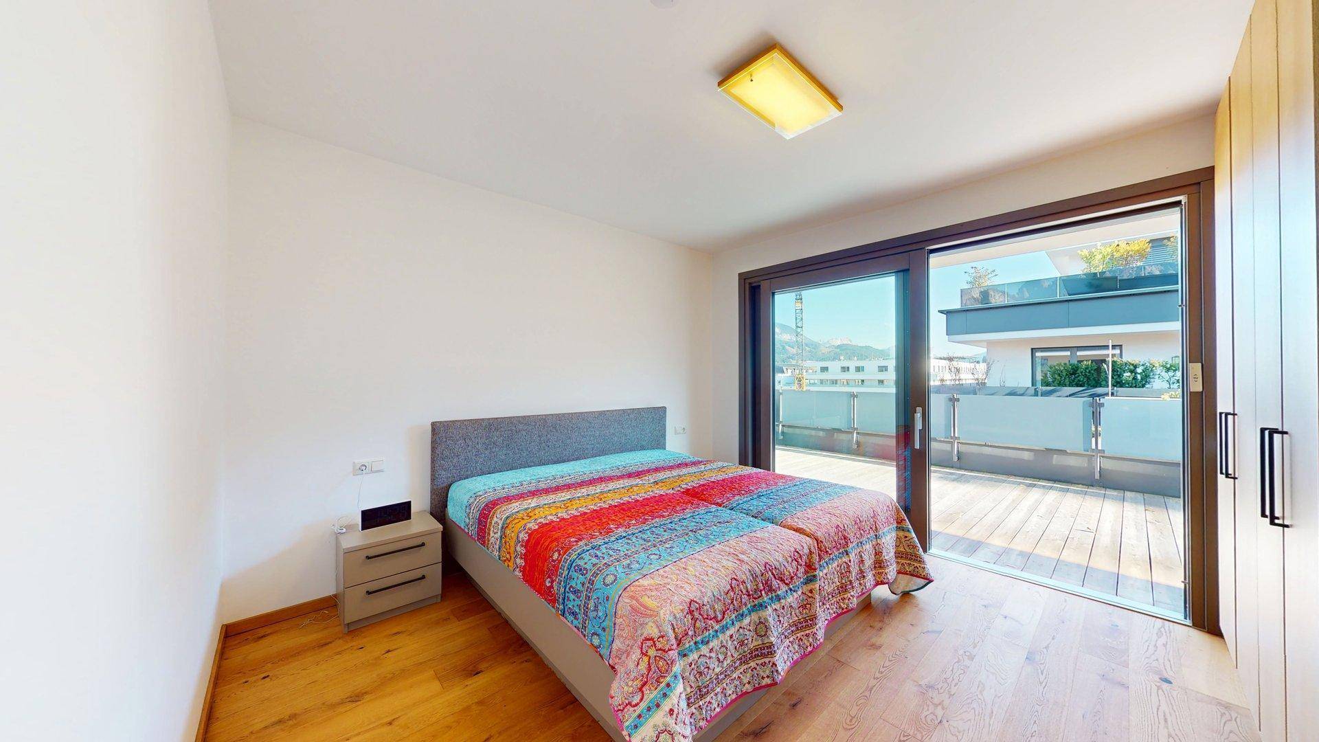 Schlafzimmer mit Holzboden, Doppelbett und direktem Zugang zu einer sonnigen Außenterrasse.